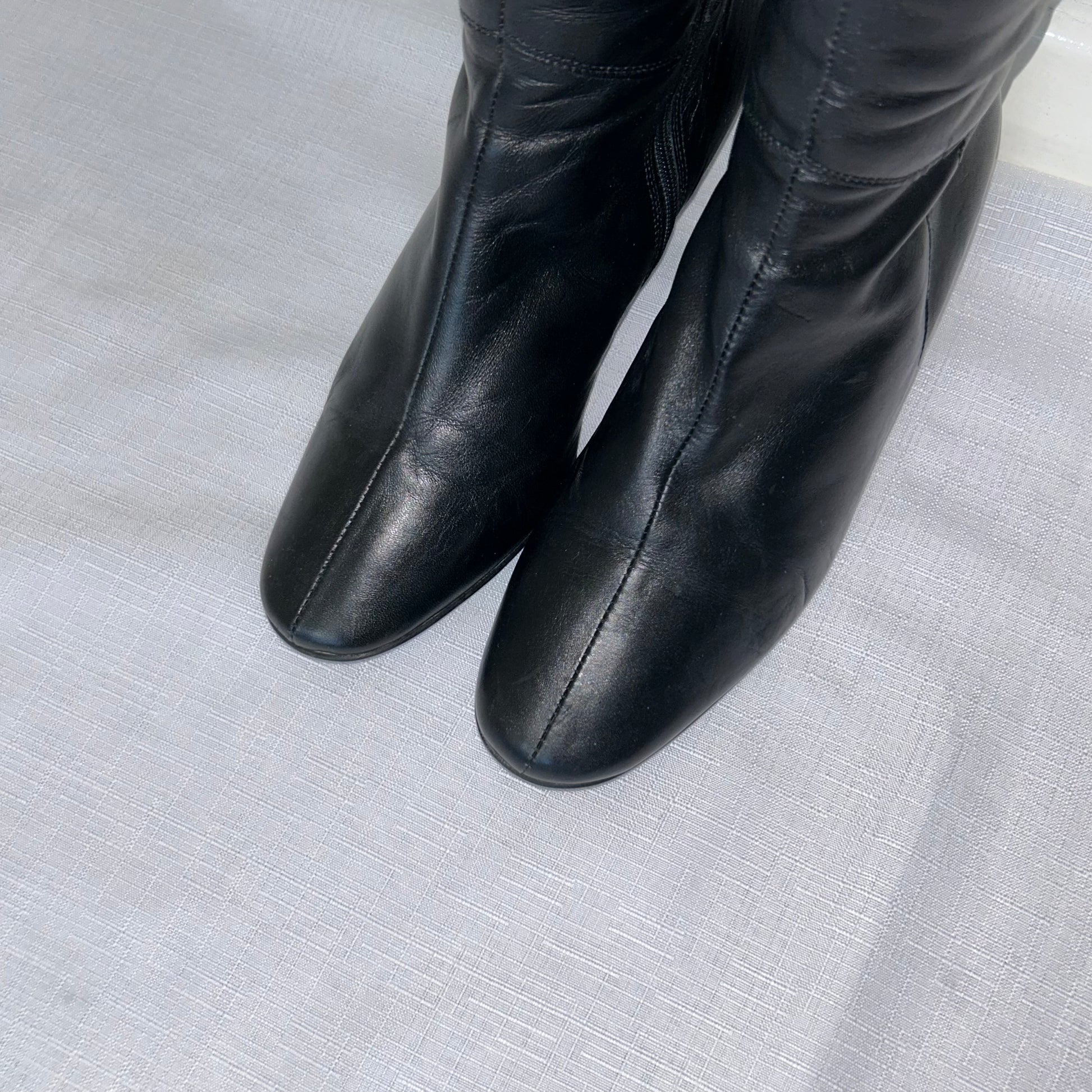toes of black knee high kitten heel leather boots shown on a white background