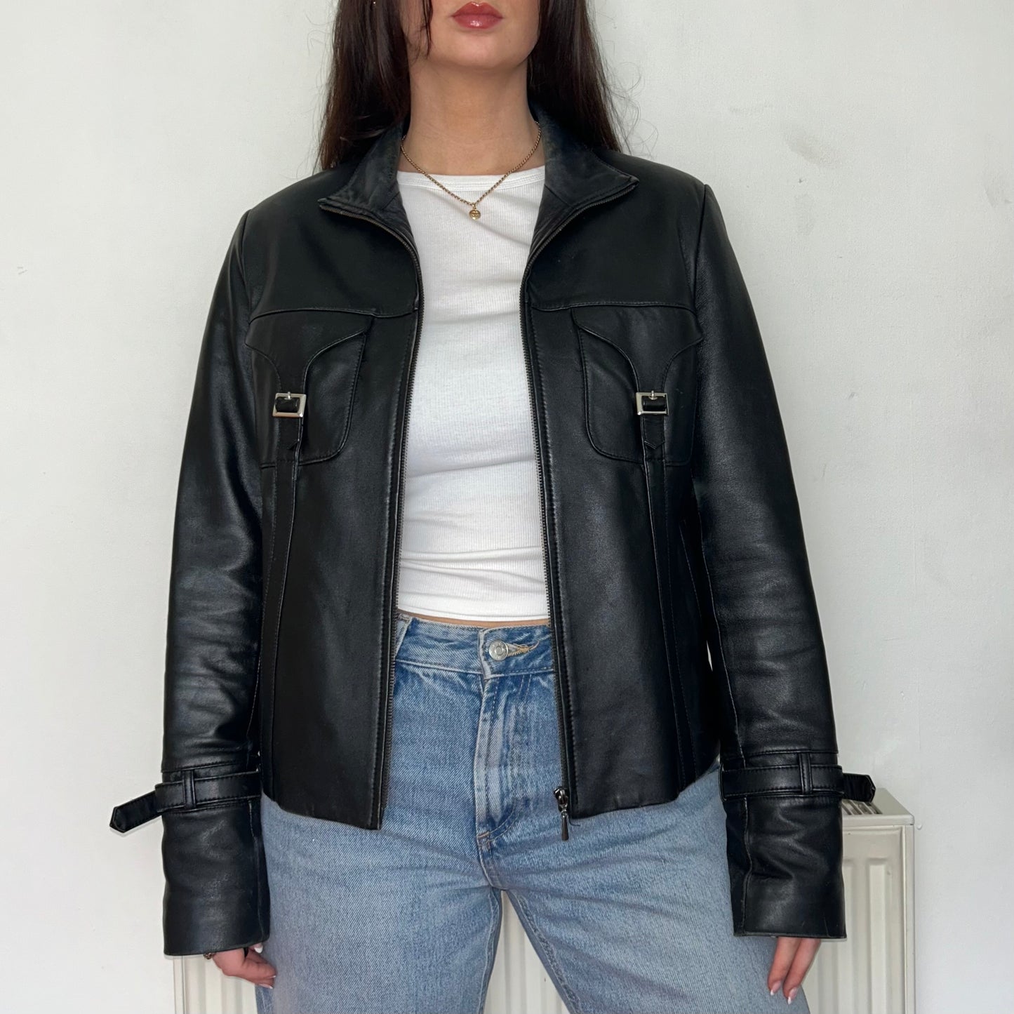 close up of black leather buckle bomber jacket shown on a model wearing a white crop top and blue jeans