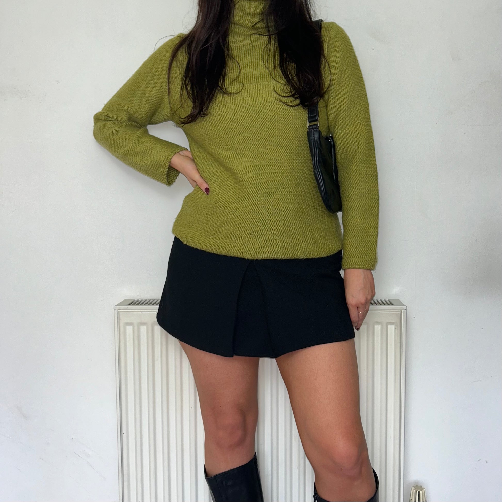green high neck knit jumper shown on a model wearing a black mini skirt and black shoulder bag  and black  boots