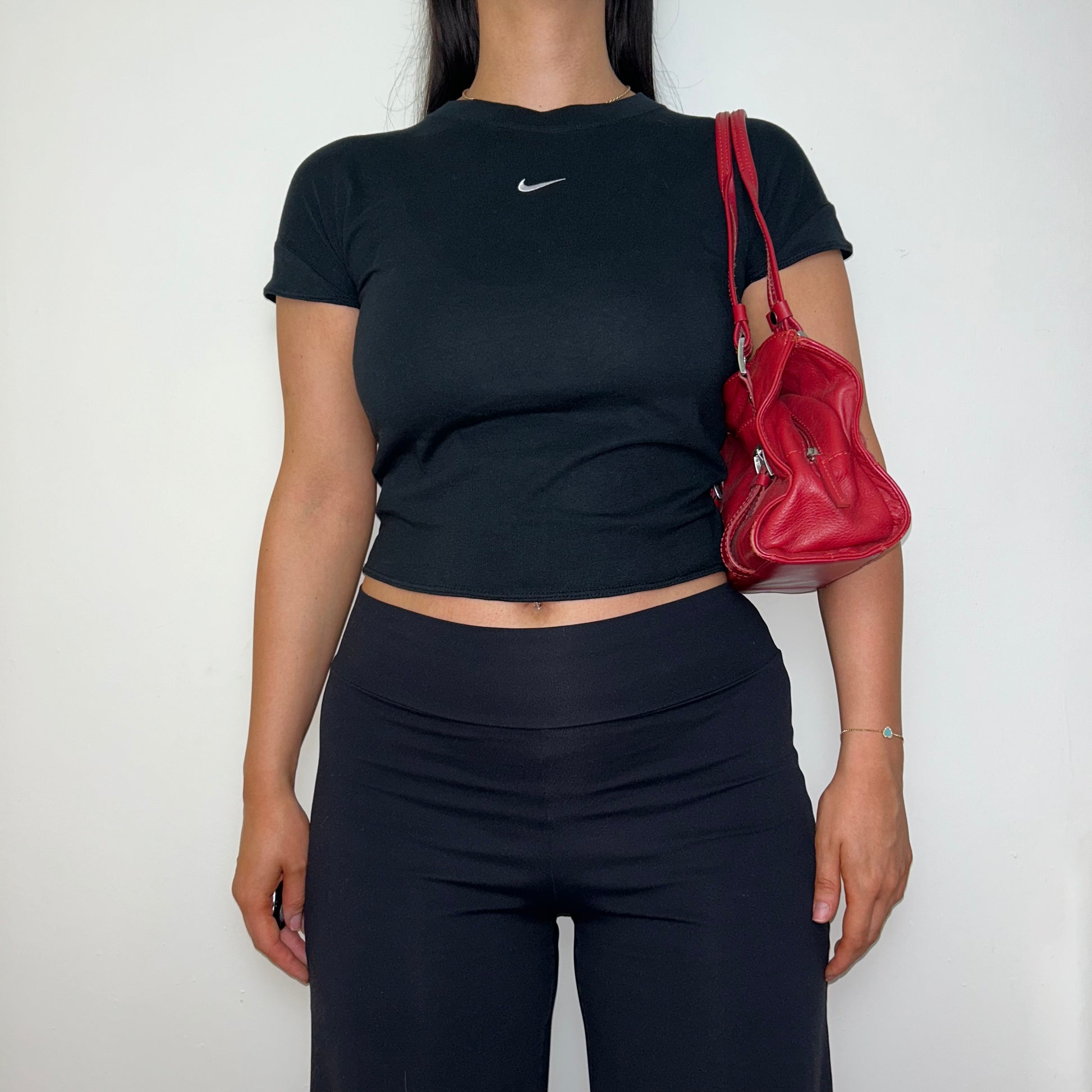 black short sleeve crop top with white nike swoosh logo shown on a model wearing black trousers and a red shoulder bag