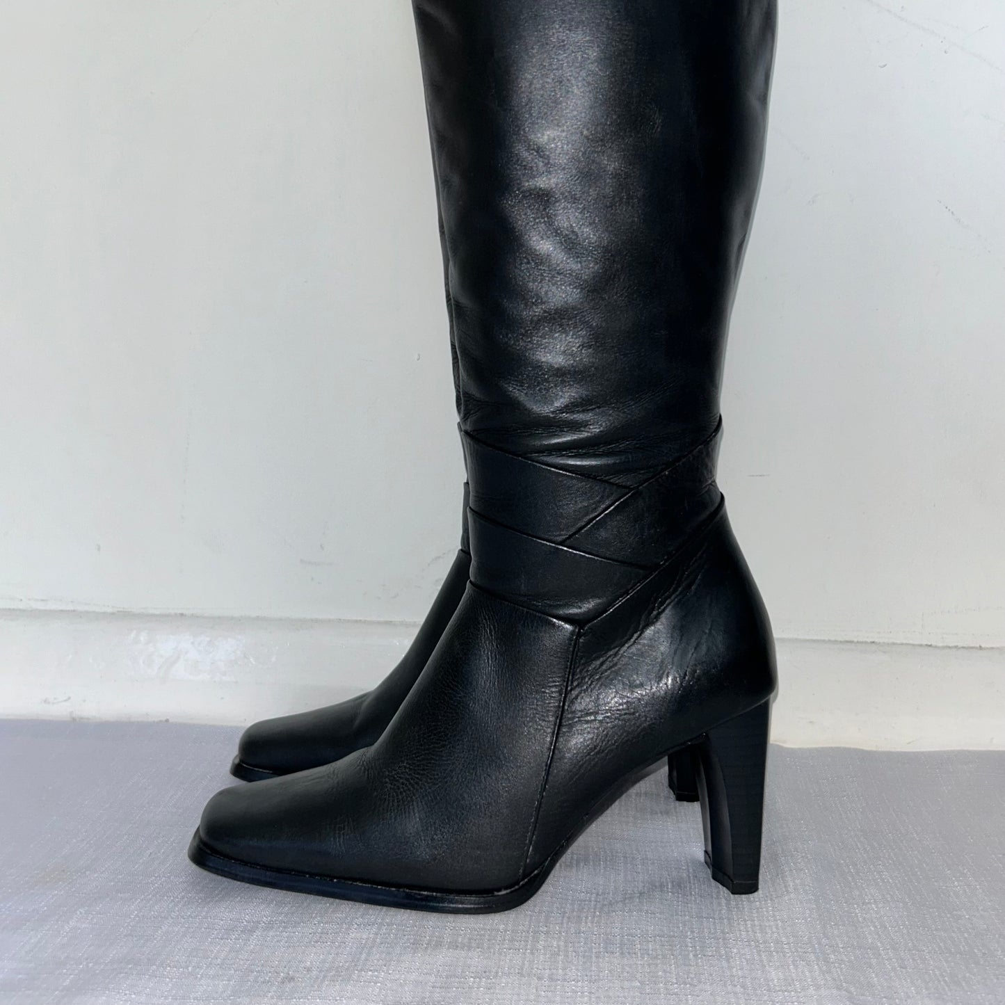 close up of black knee high leather boots on a white background