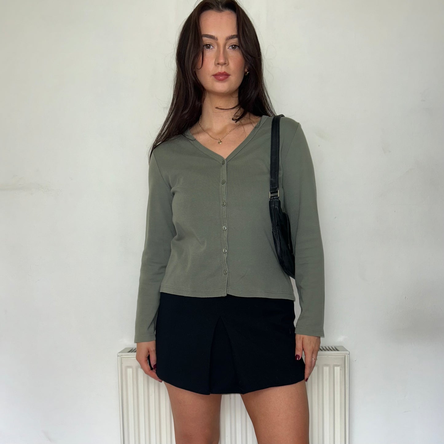 green button up long sleeve top shown on a model wearing a black skirt and a black bag