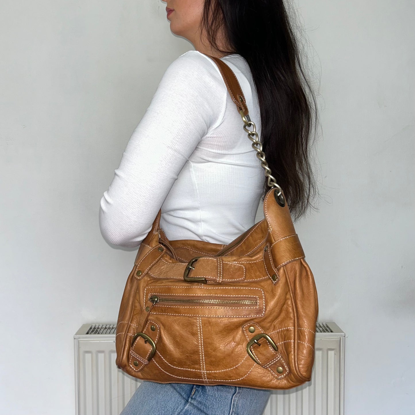 tan brown leather shoulder bag shown on a models shoulder wearing a white top and blue jeans