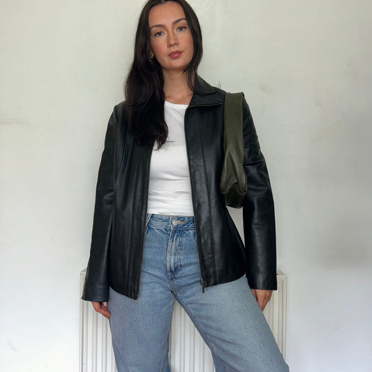 black leather bomber jacket shown on a model wearing a white top and blue jeans with a green bag