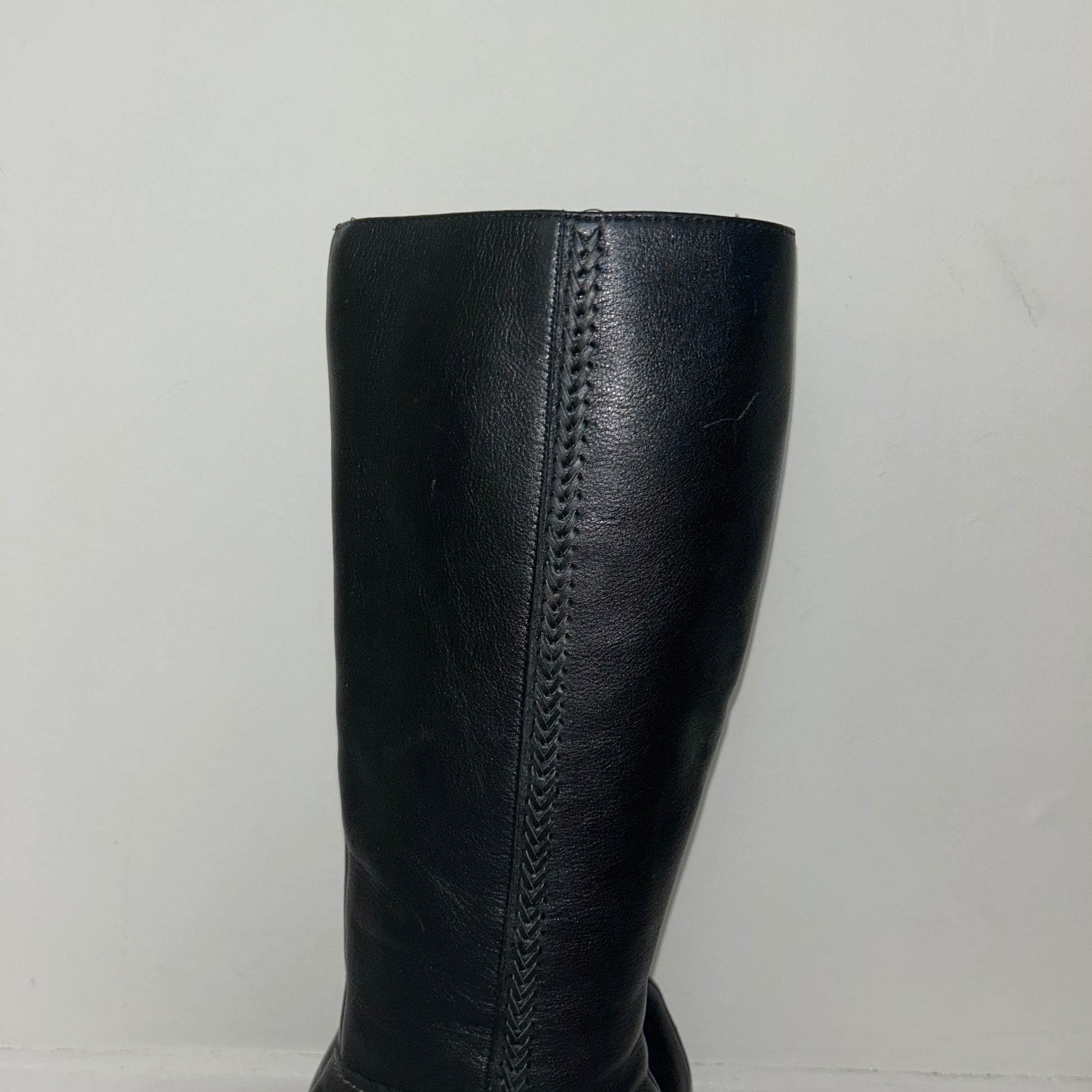 close up of black knee high real leather boots shown on a white background
