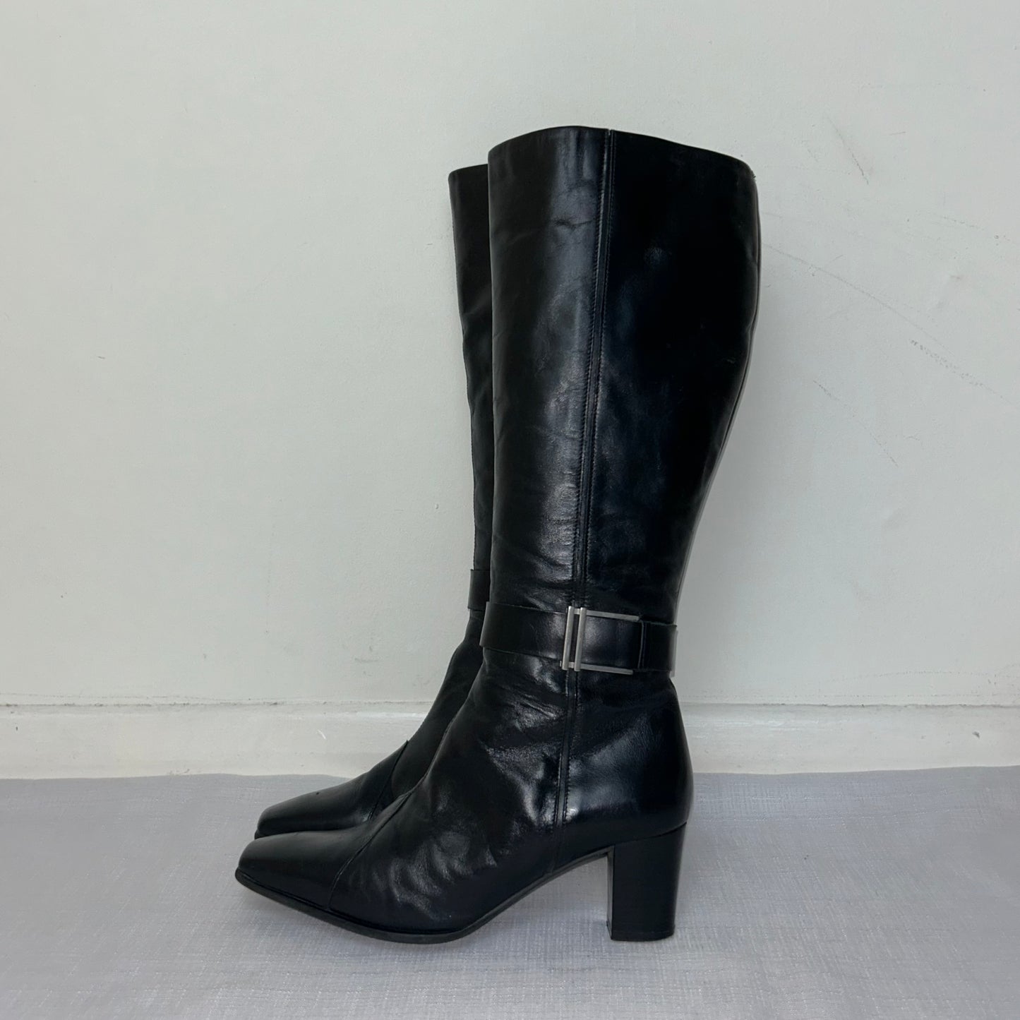 black knee high leather boots with silver buckle shown on a white background