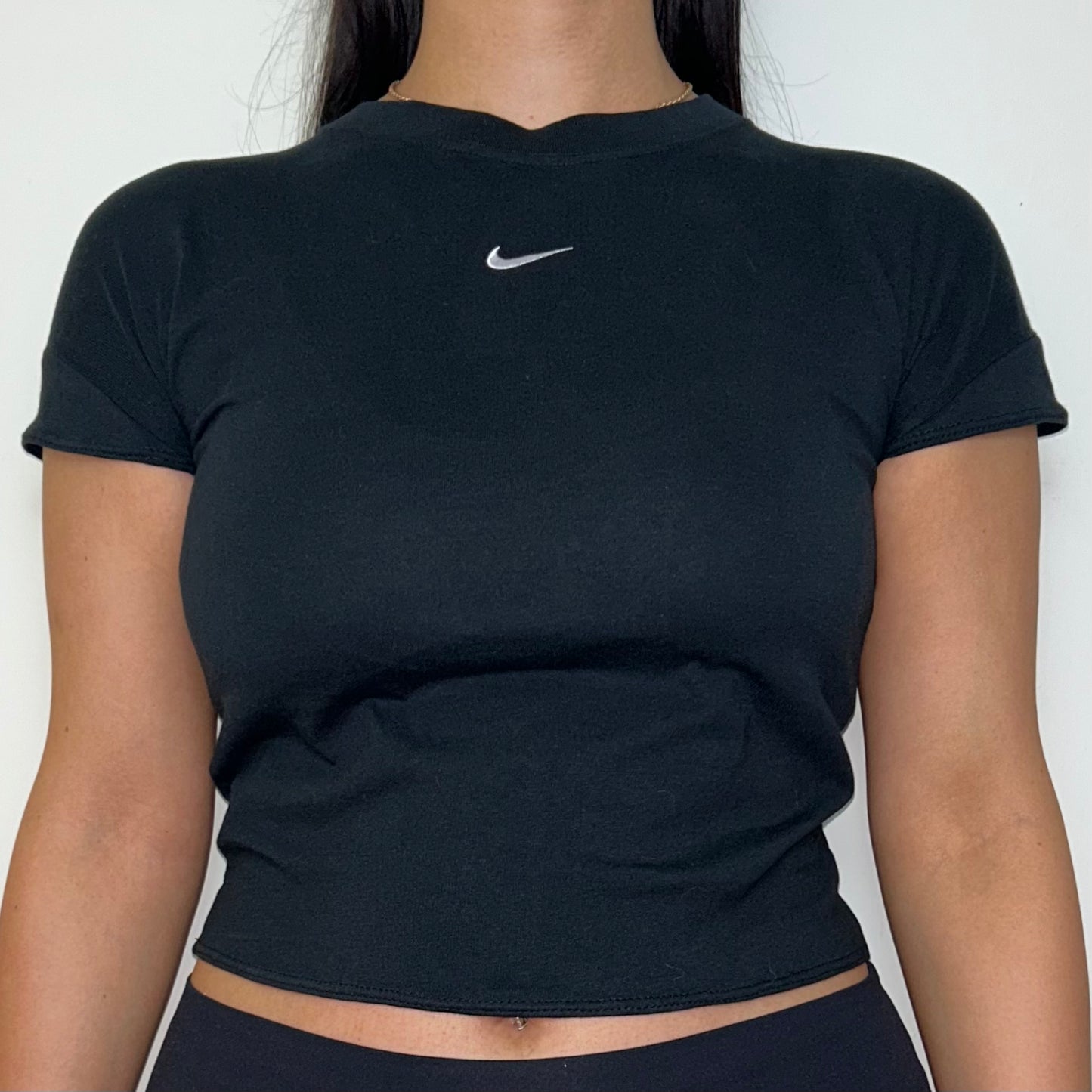 close up of black short sleeve crop top with white nike swoosh logo shown on a model wearing black trousers