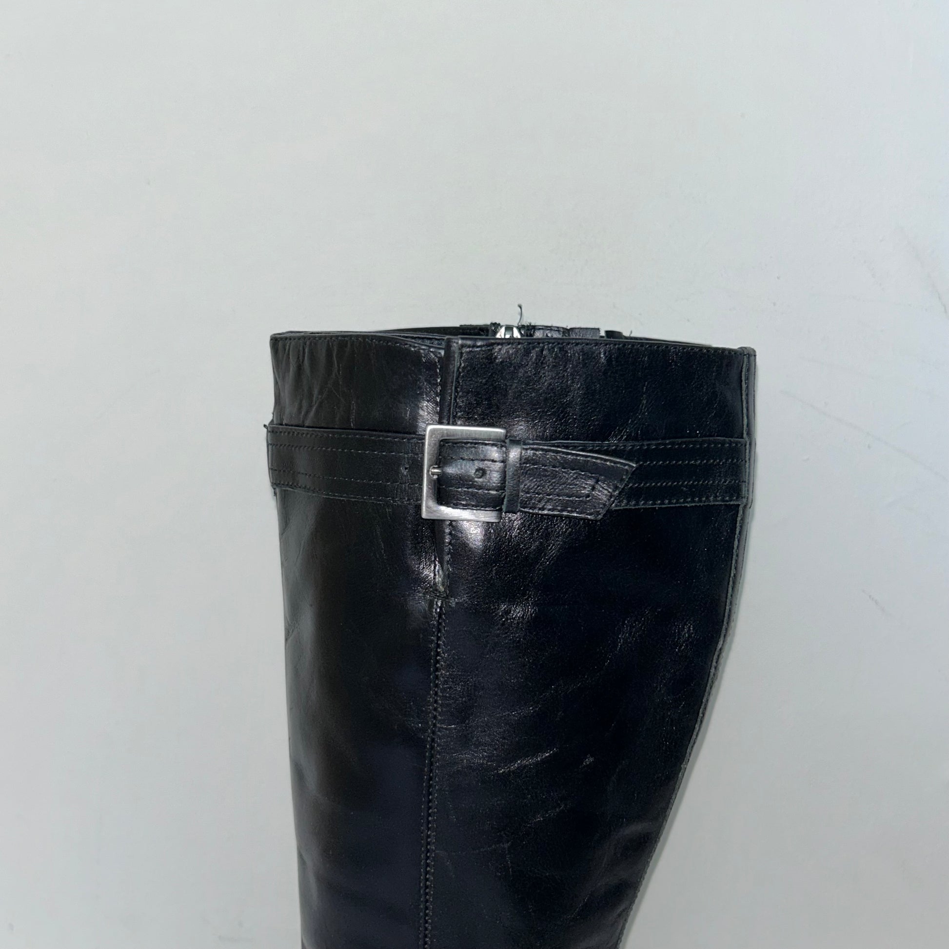 close up of black knee high block heel leather boots shown on a white background