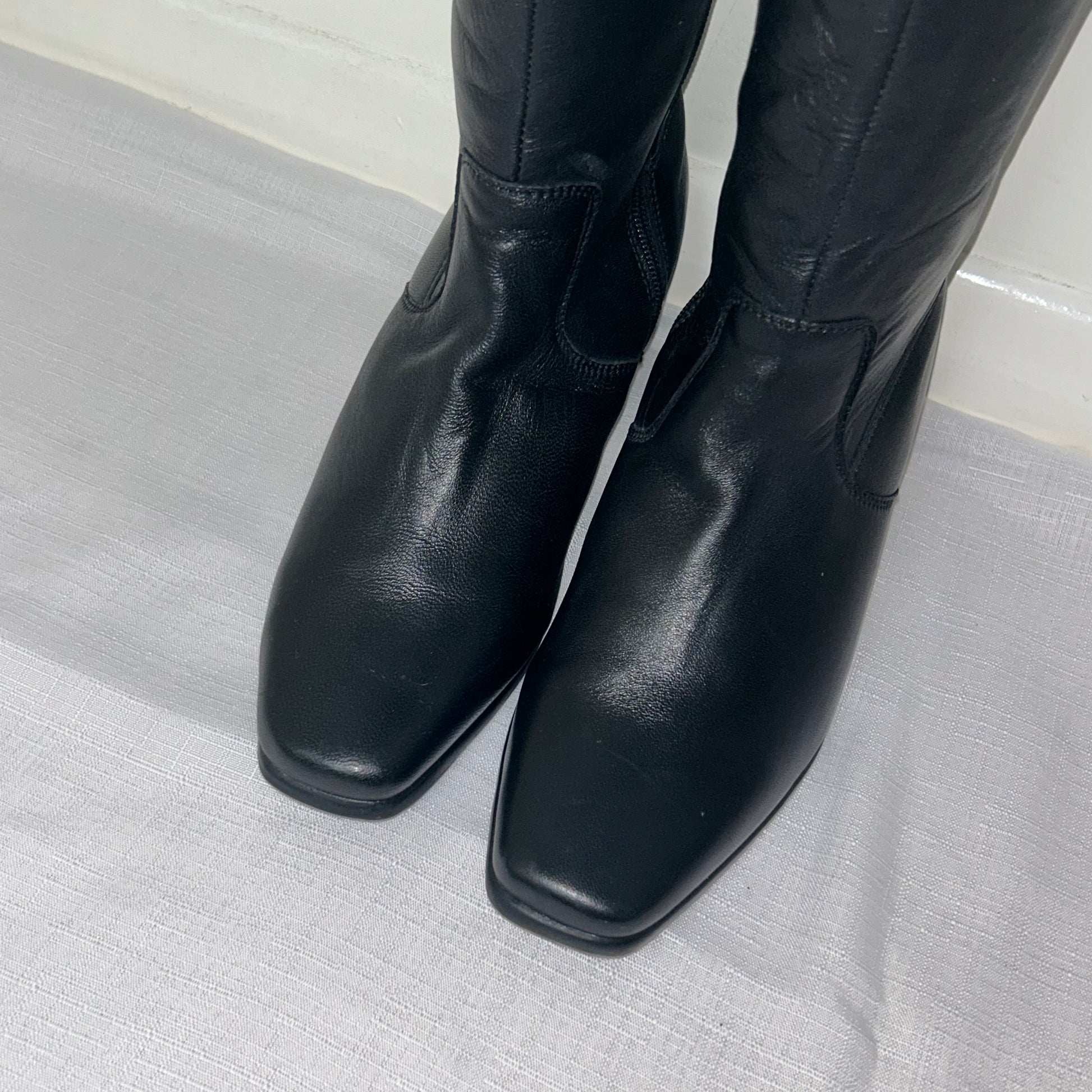 toes of black knee high silver buckle boots shown on a white background
