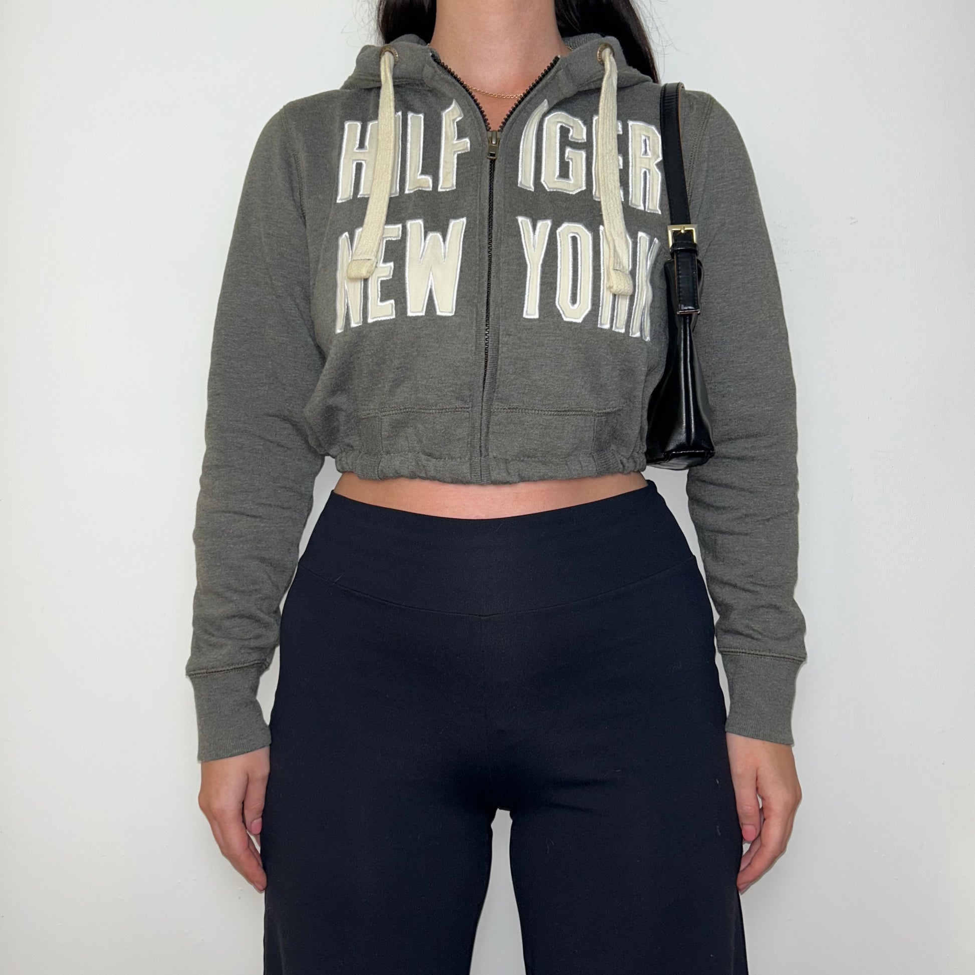 grey tommy hilfiger cropped hoodie shown on a model wearing black trousers and a black shoulder bag