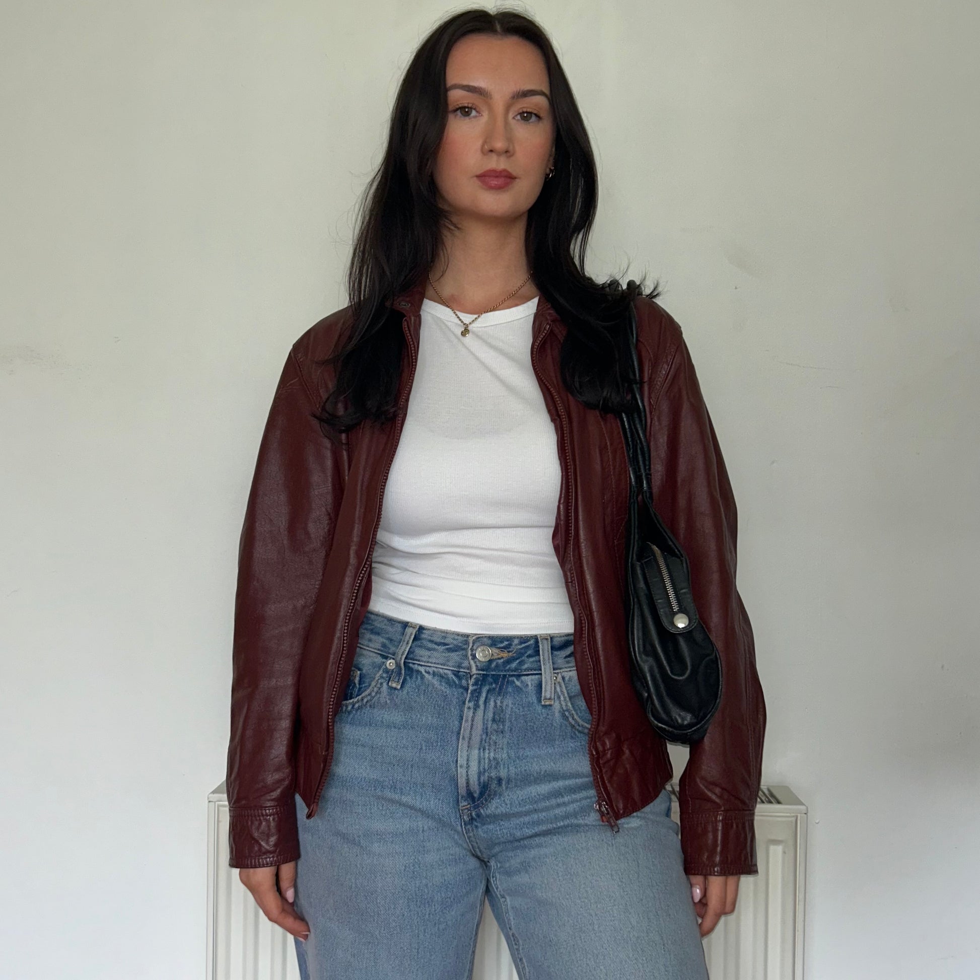 burgundy vintage leather jacket shown on a model wearing a white top and blue jeans and a black bag