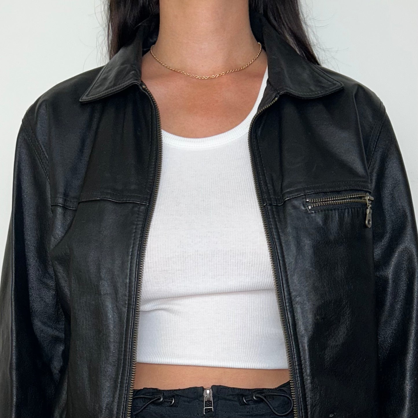 close up of black real leather bomber jacket shown on a model wearing a white crop top and black mini skirt