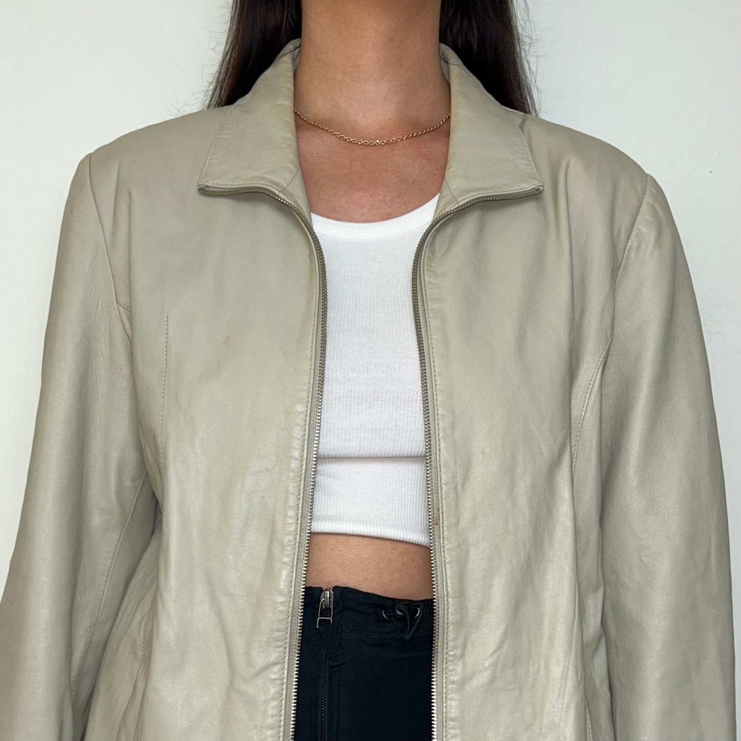 close up of beige leather zip up jacket shown on a model wearing a white crop top and black skirt