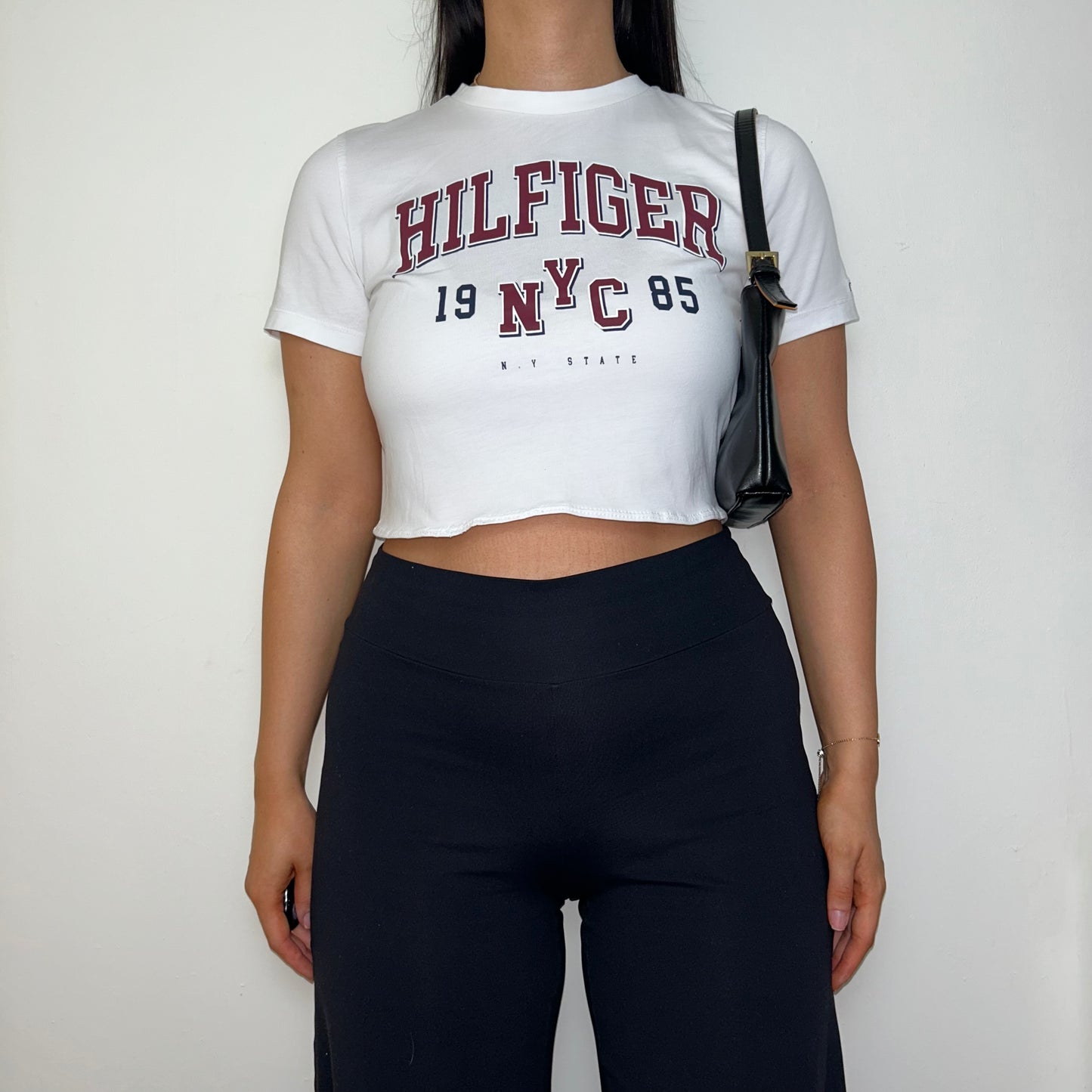 white short sleeve crop top with hilfiger logo shown on a model wearing black trousers and a black shoulder bag