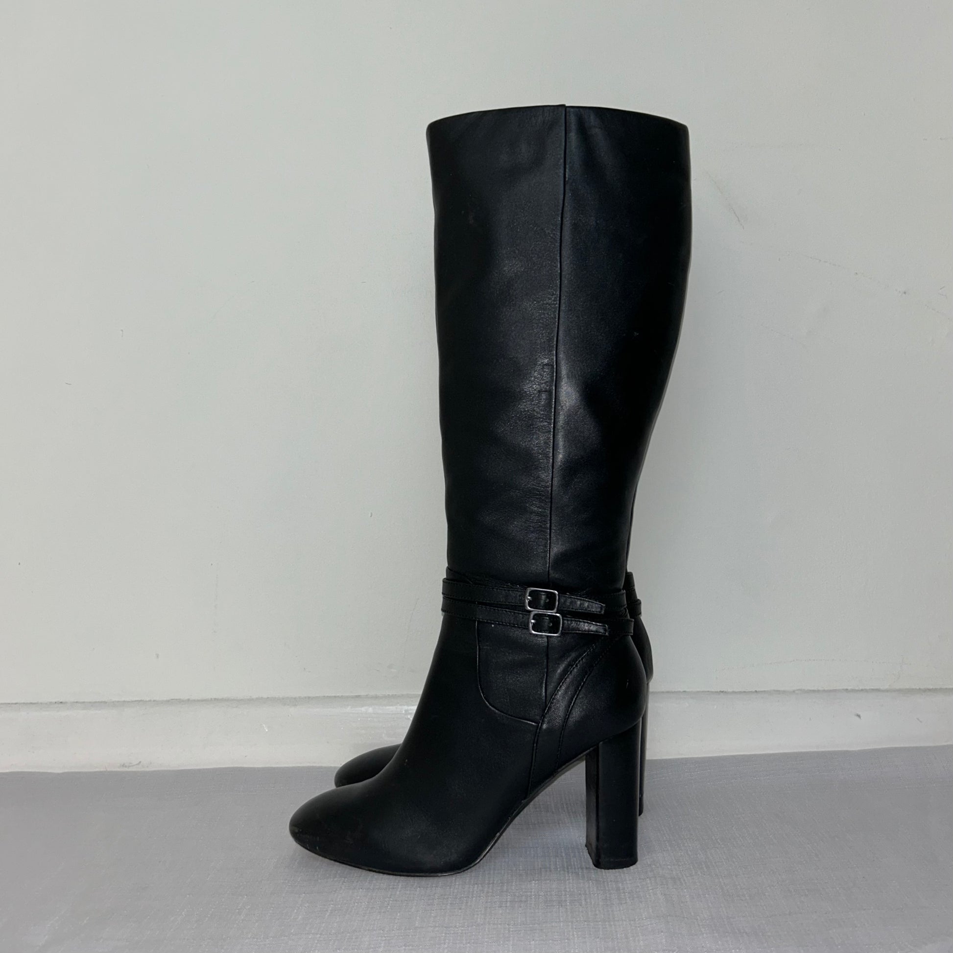 black knee high buckle boots shown on a white background