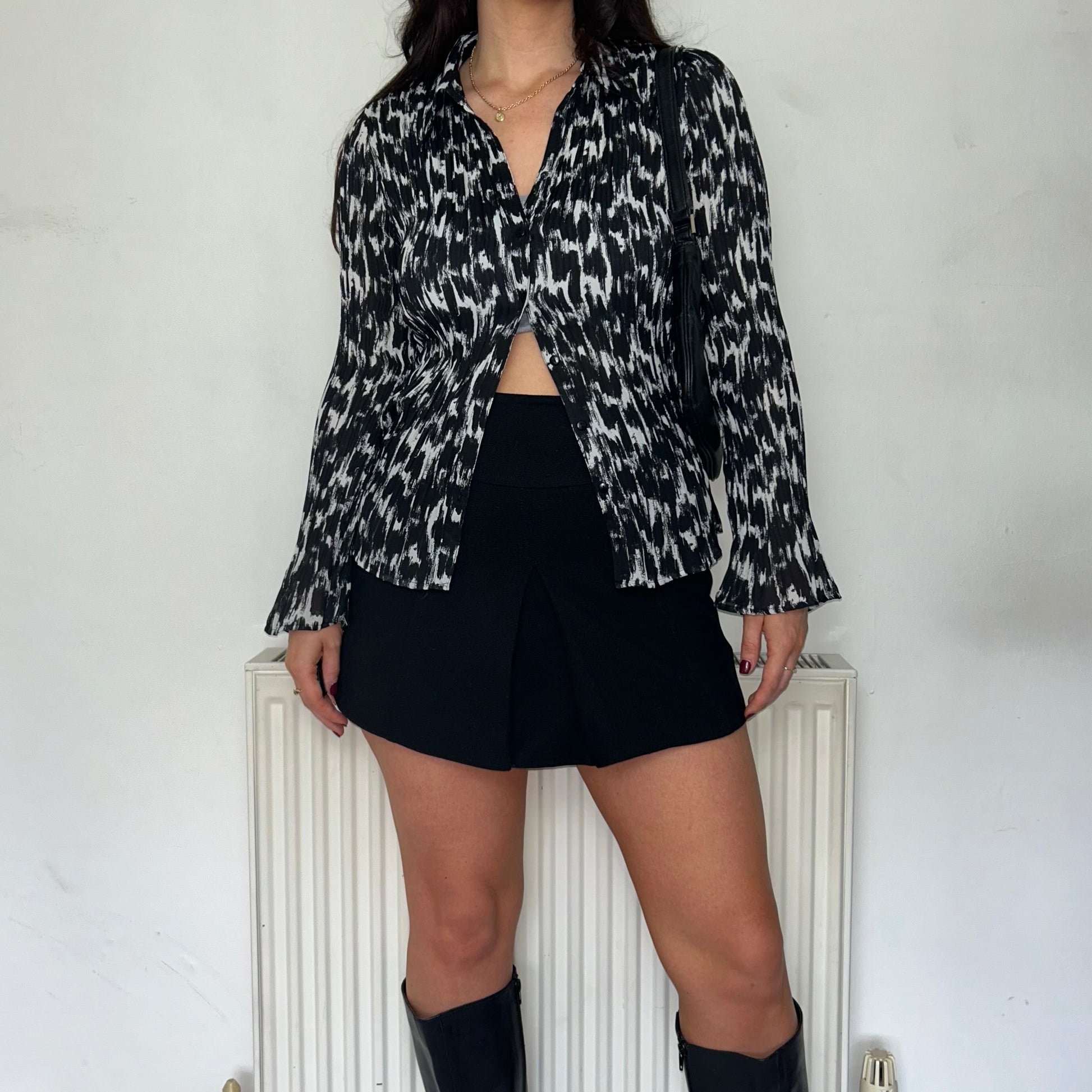 black an white blouse shown on a model wearing a black mini skirt and black boots with a black shoulder bag