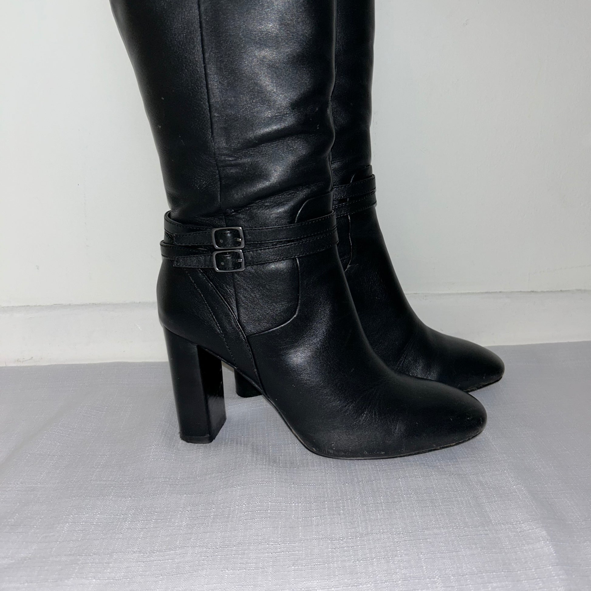 close up of buckles on black knee high buckle boots shown on a white background