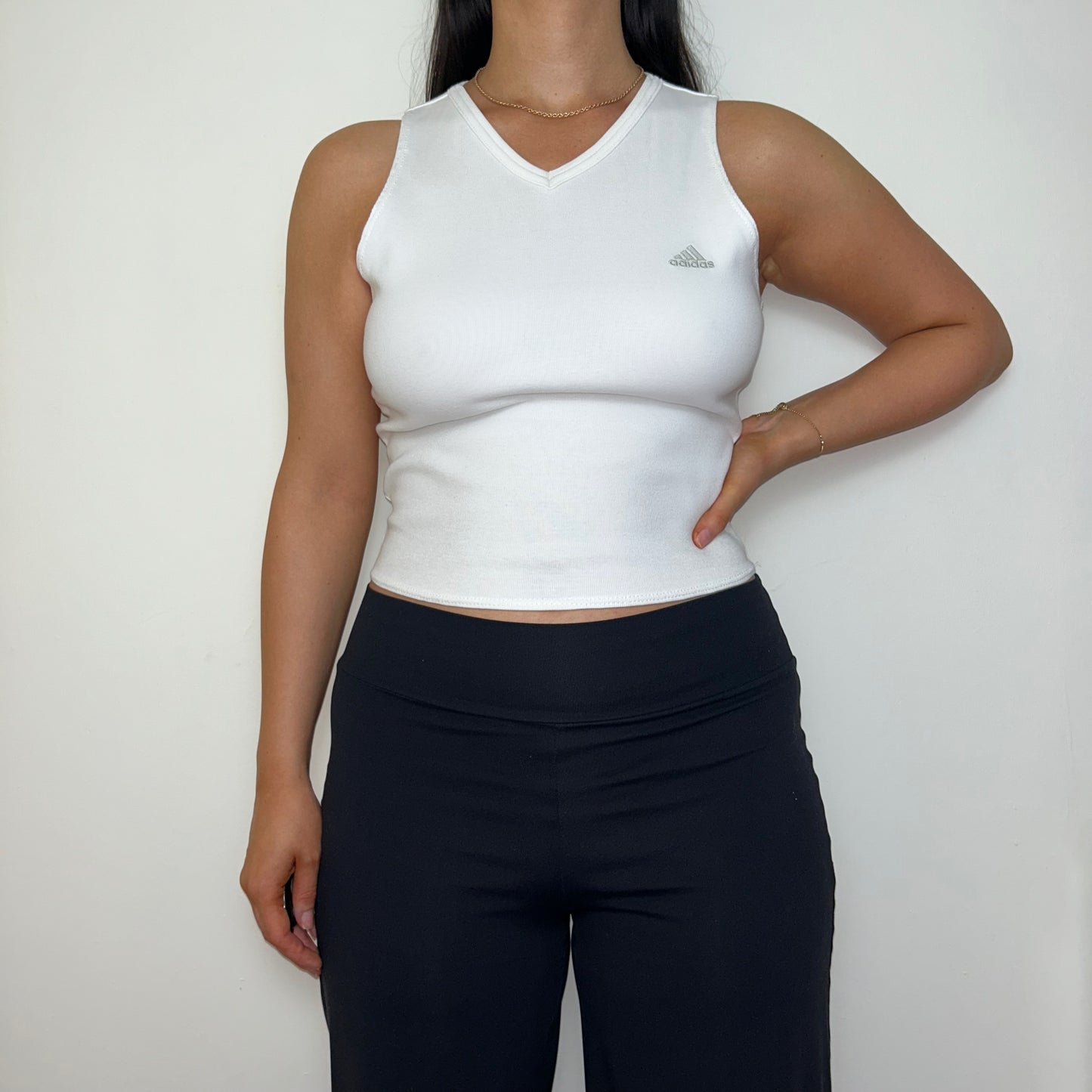 white sleeveless crop top with grey adidas logo shown on a model wearing black trousers