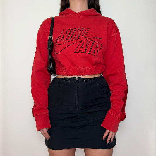 red cropped hoodie with black nike air logo shown on a model wearing a black mini skirt and black shoulder bag