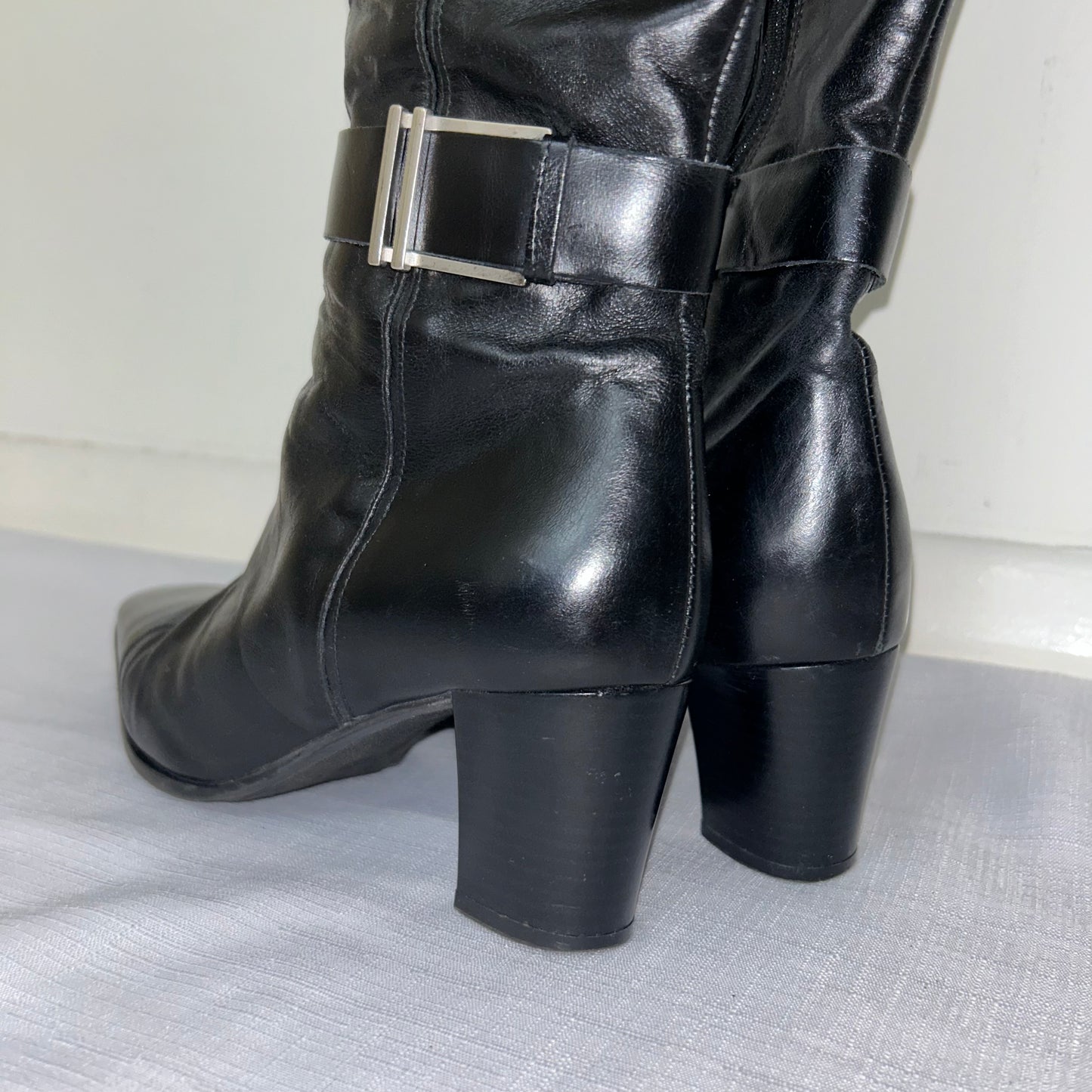 heels of black knee high leather boots with silver buckle shown on a white background