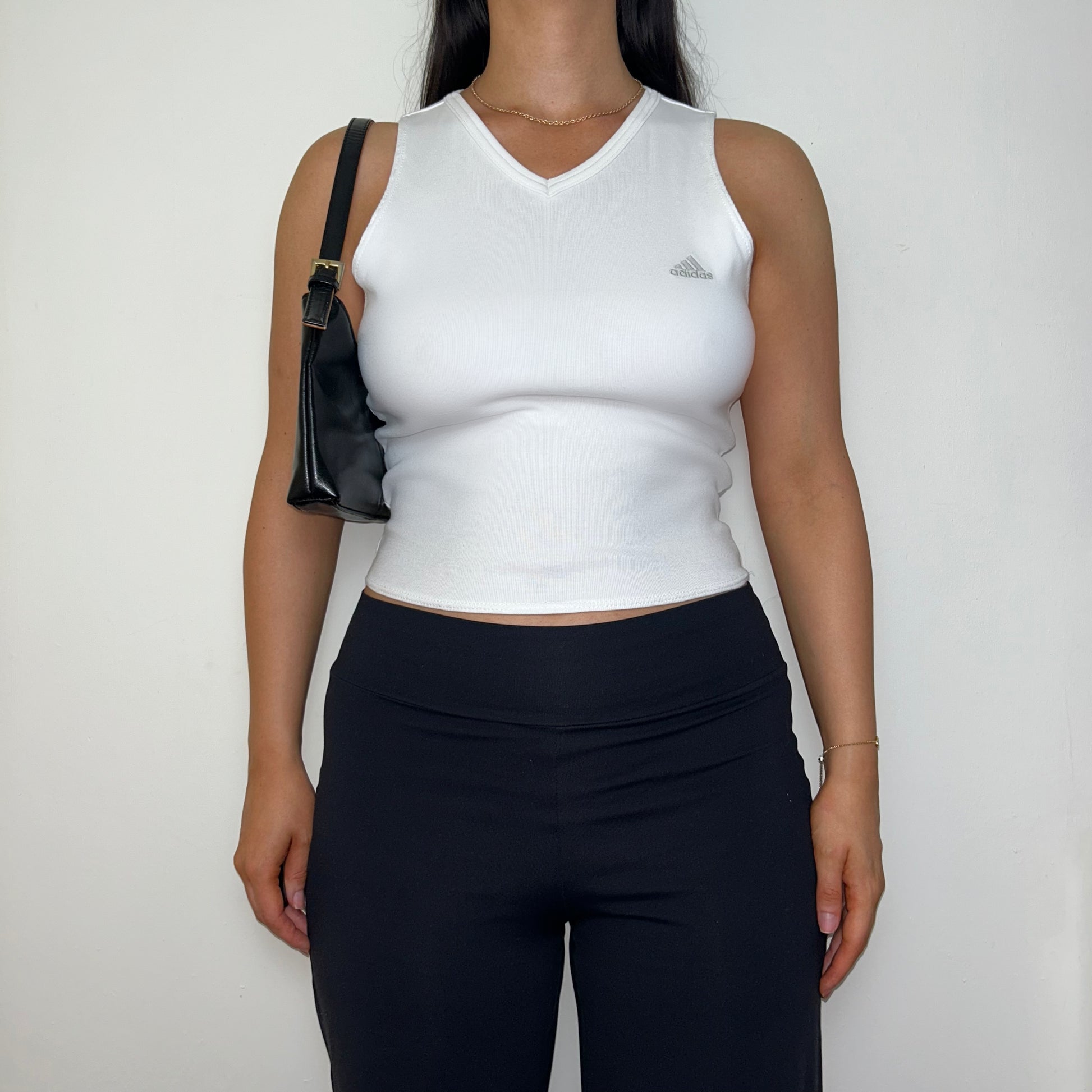 white sleeveless crop top with grey adidas logo shown on a model wearing black trousers and a black shoulder bag