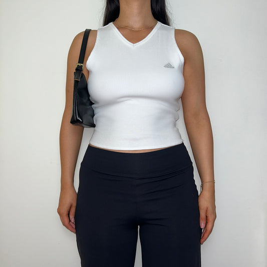 white sleeveless crop top with grey adidas logo shown on a model wearing black trousers and a black shoulder bag