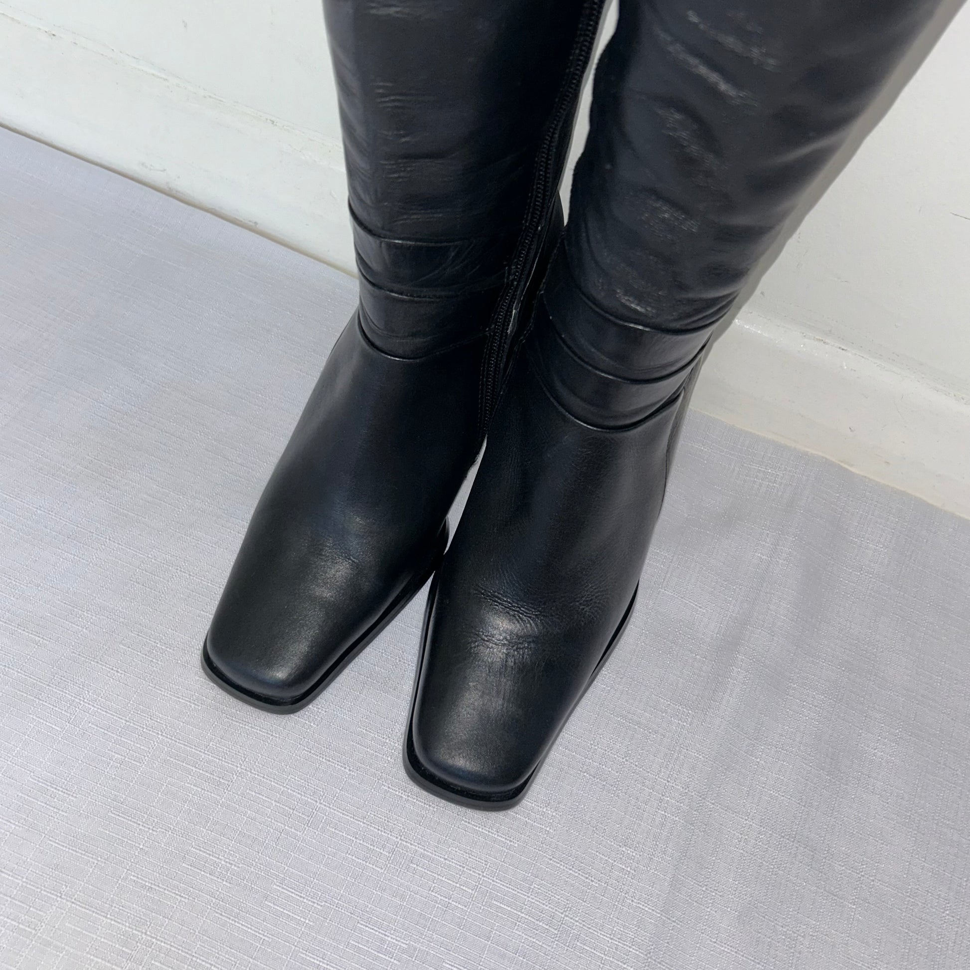 toes of black knee high leather boots on a white background