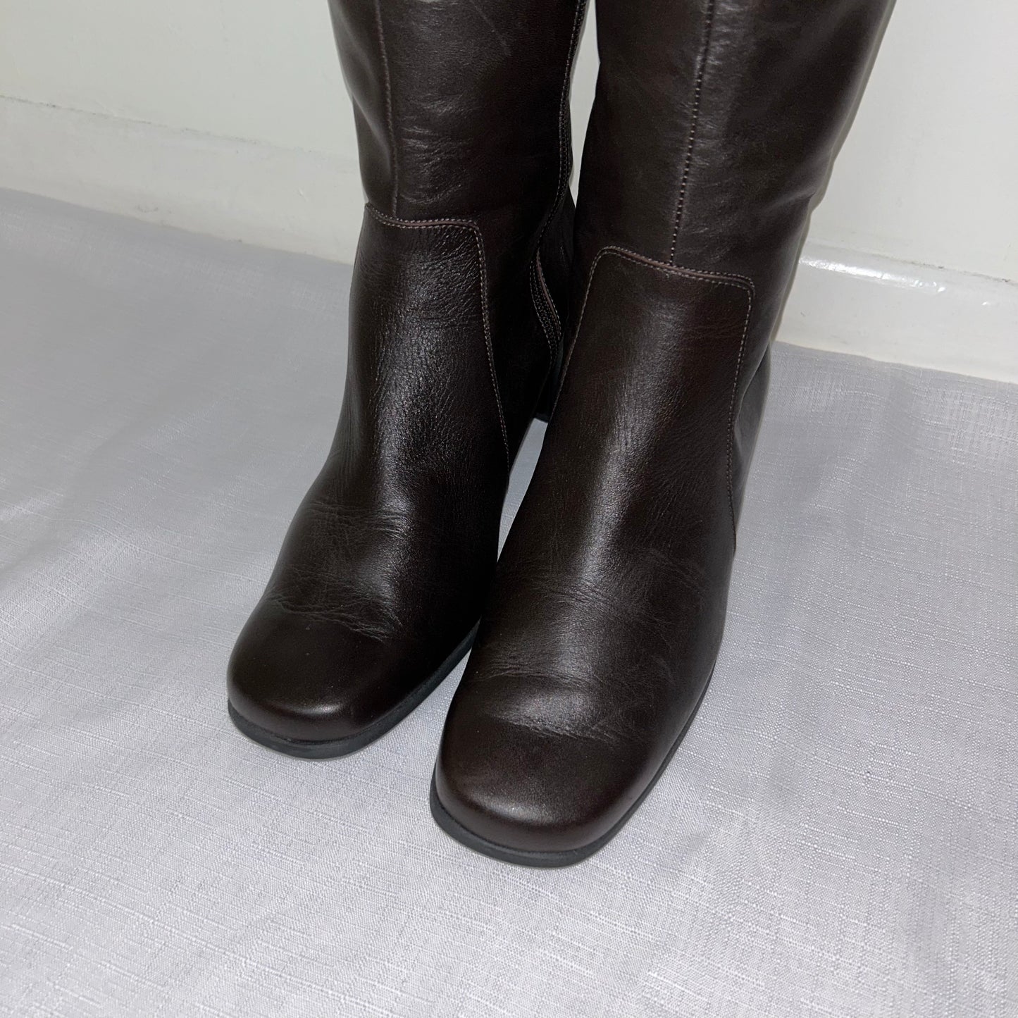 toes of dark brown leather knee high boots shown on a white background
