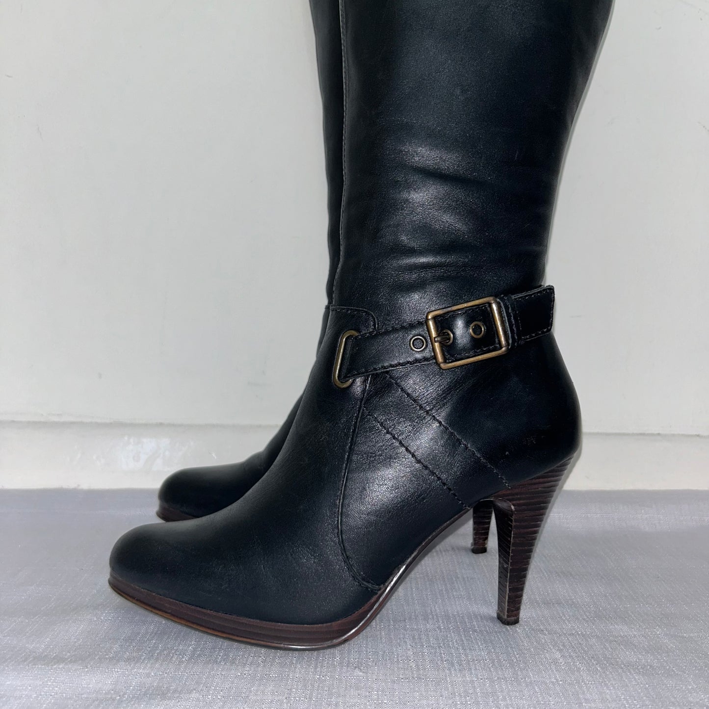 close up of black knee high buckle boots shown on a white background