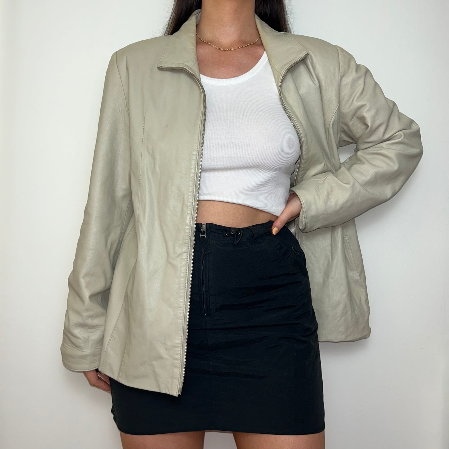 beige leather zip up jacket shown on a model wearing a white crop top and black skirt