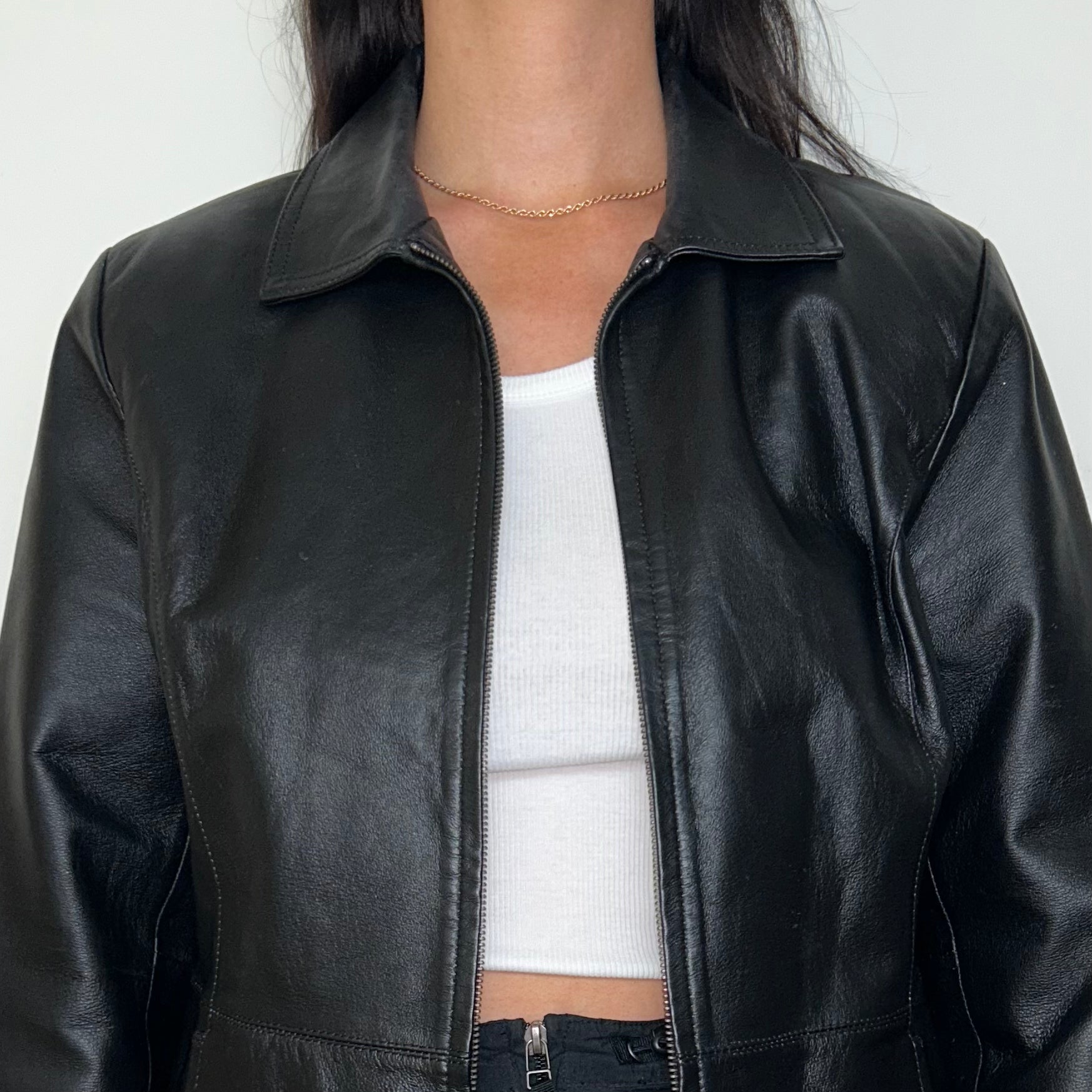 close up of black zip up bomber jacket shown on a model wearing a white crop top and black mini skirt