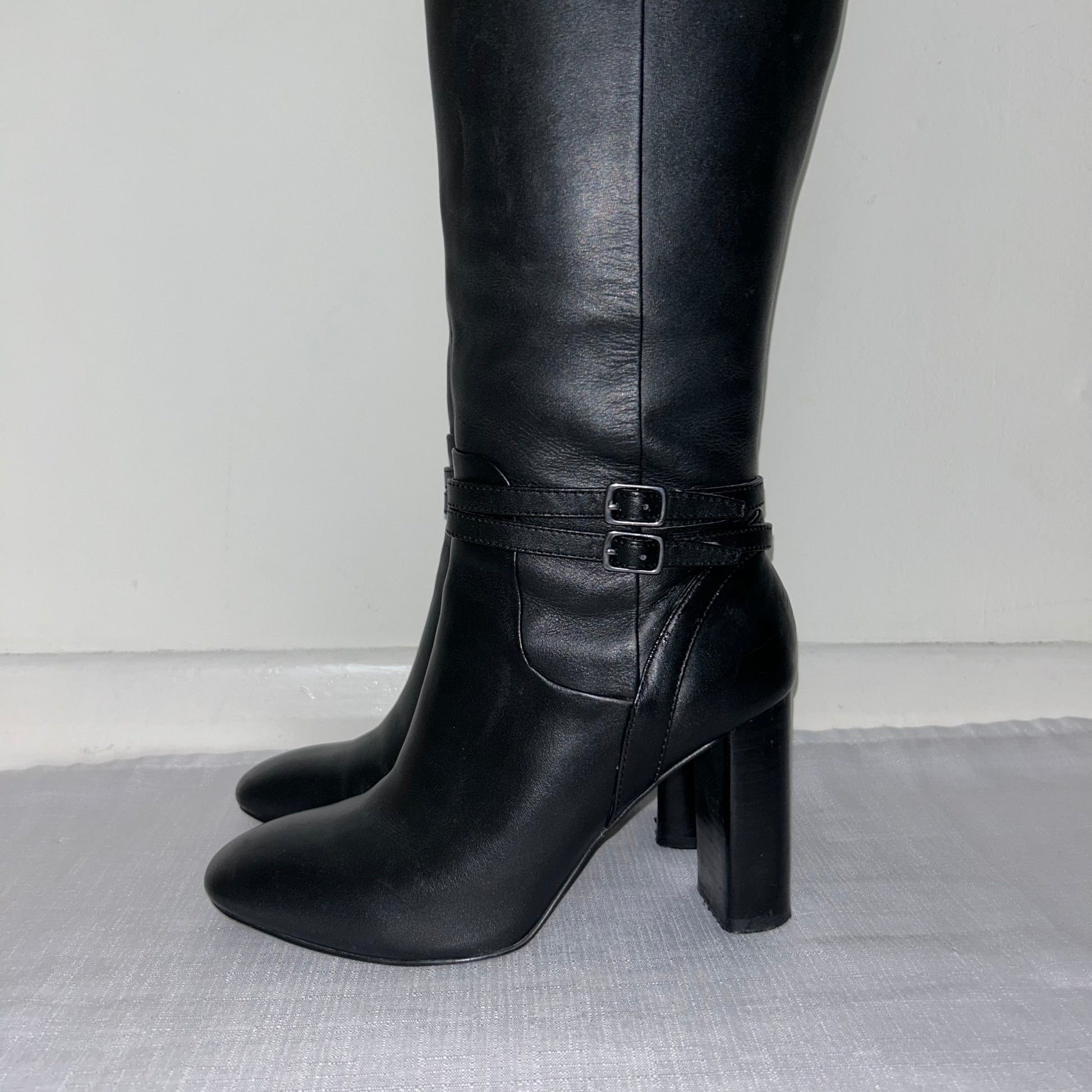 close up of black knee high boots with double silver buckle shown on a white background