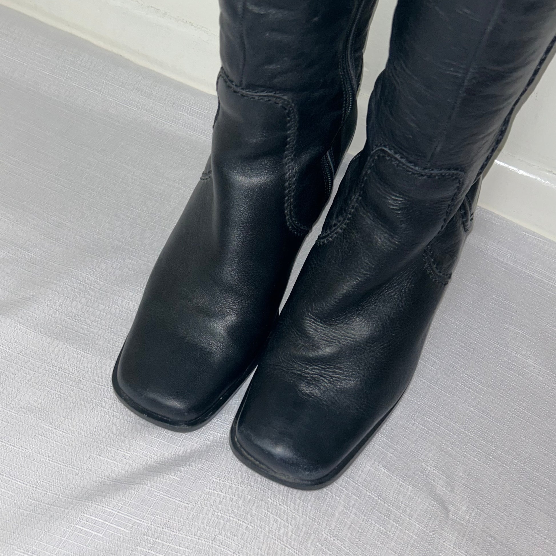 toes of black knee high boots shown on a white background