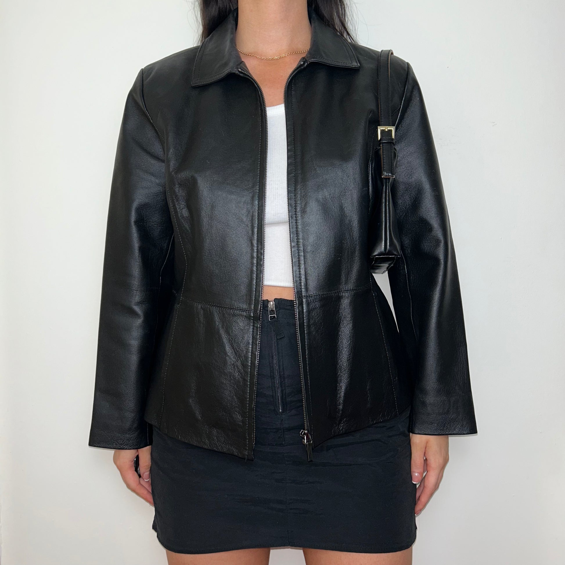 black zip up bomber jacket shown on a model wearing a white crop top and black mini skirt and black shoulder bag