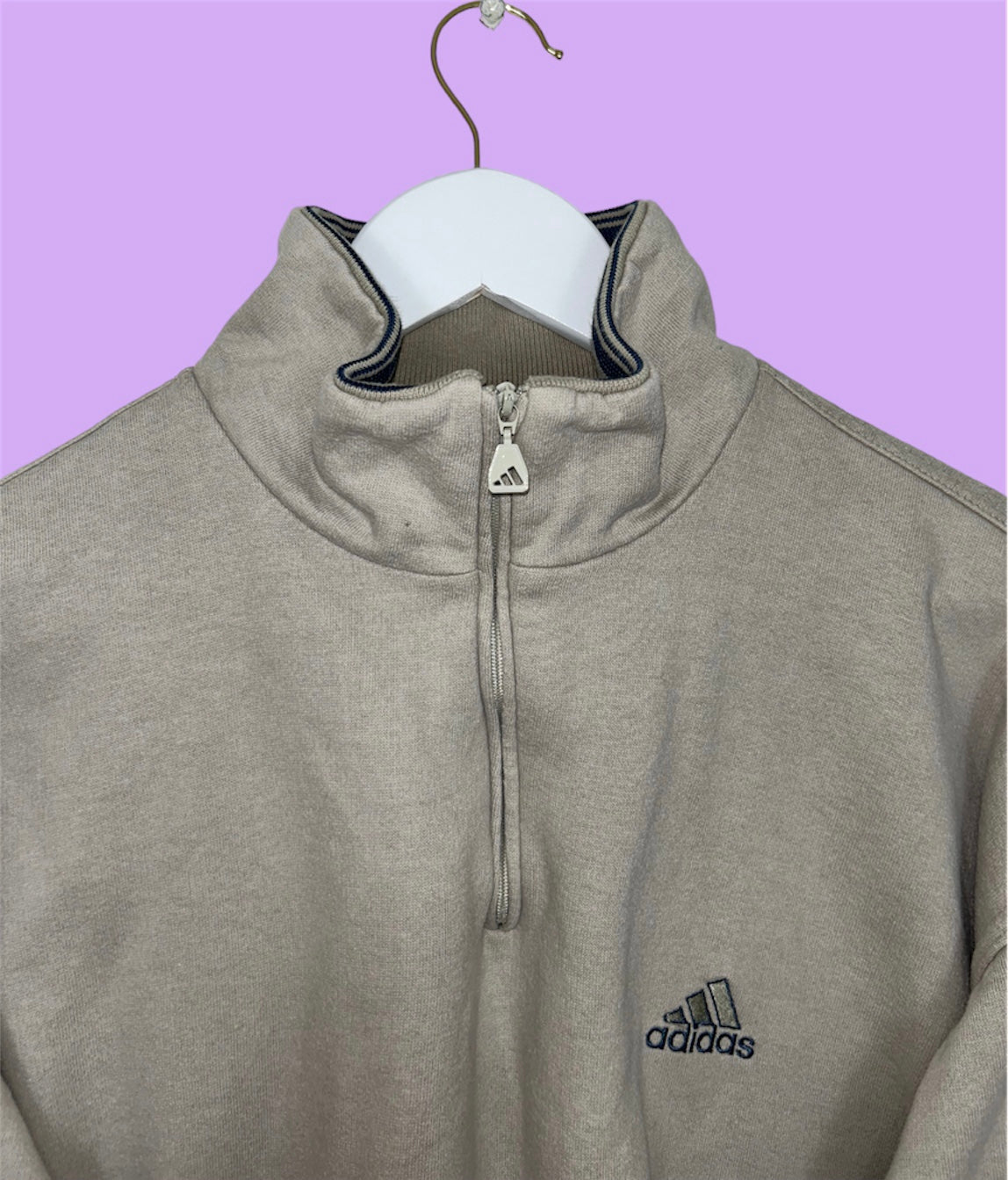 close up of beige 1/4 zip sweatshirt with small adidas logo shown on a lilac background