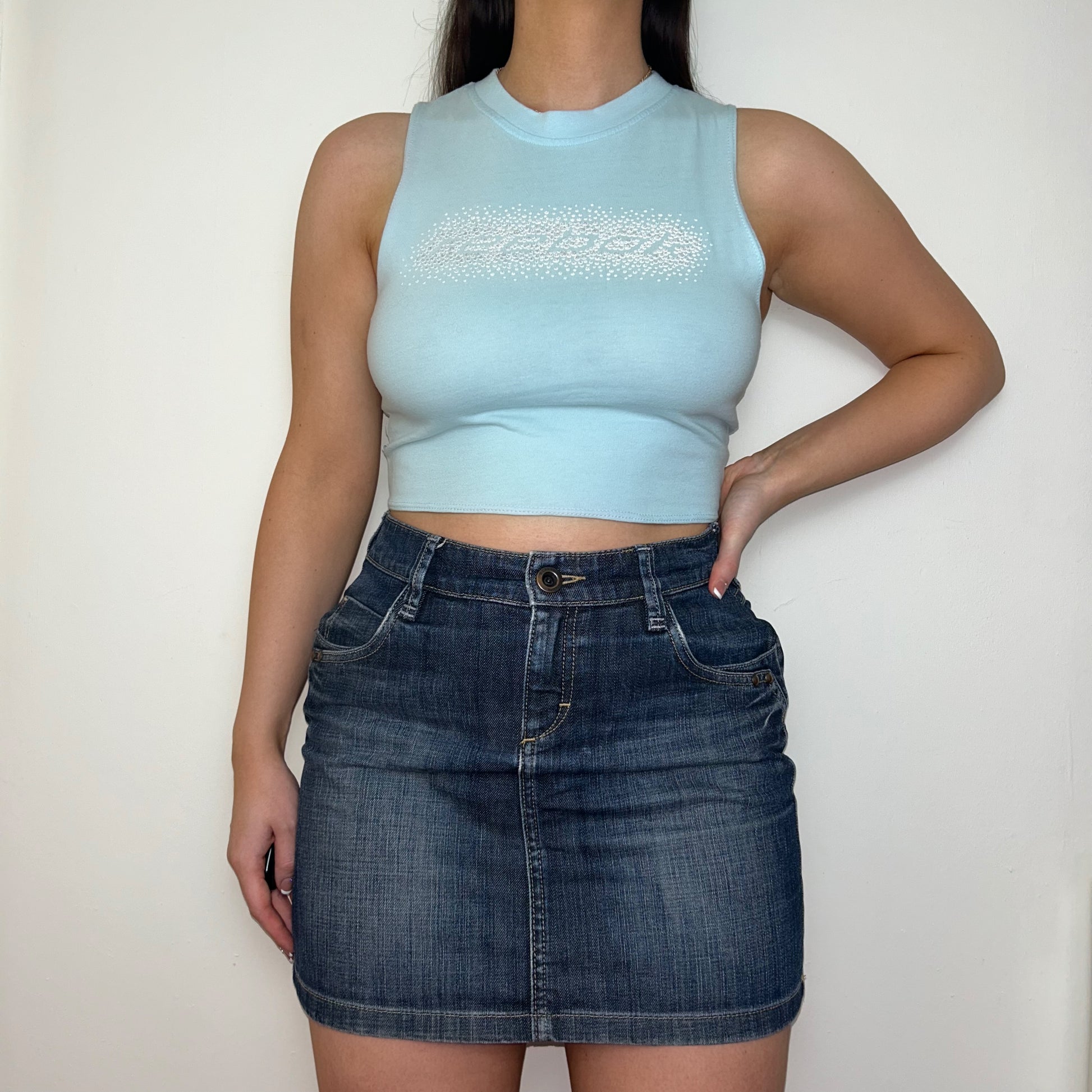 light blue sleeveless crop top with gem reebok logo shown on a model wearing a denim mini skirt