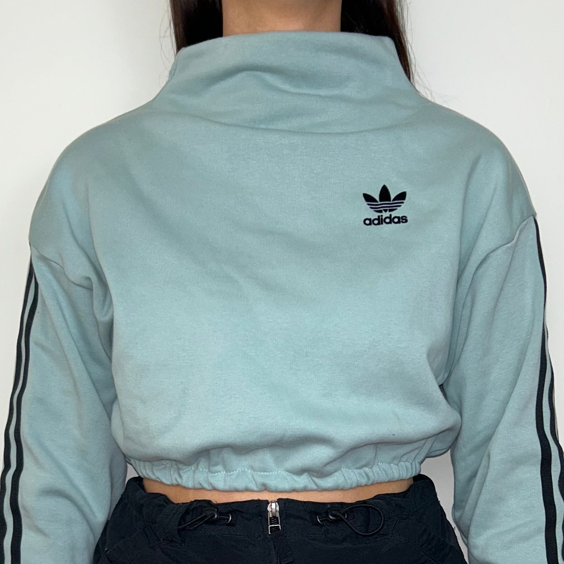 close up of light blue cropped sweatshirt with black adidas logo shown on a model