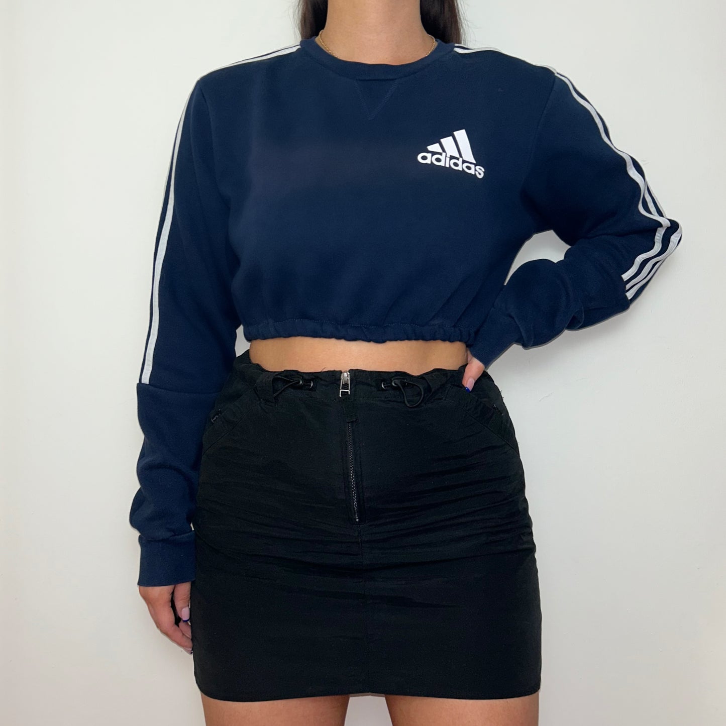 navy cropped sweatshirt with white adidas logo shown on a model wearing a black mini skirt