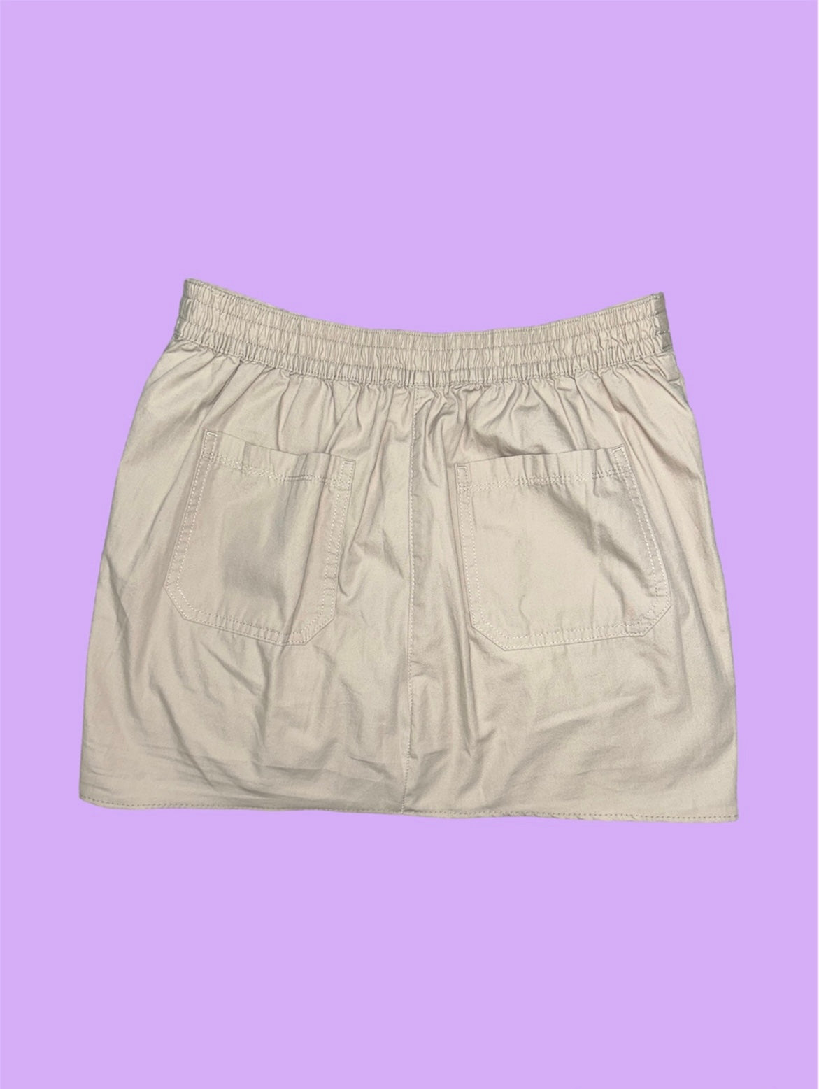 back of a beige mini cargo skirt shown on a lilac background