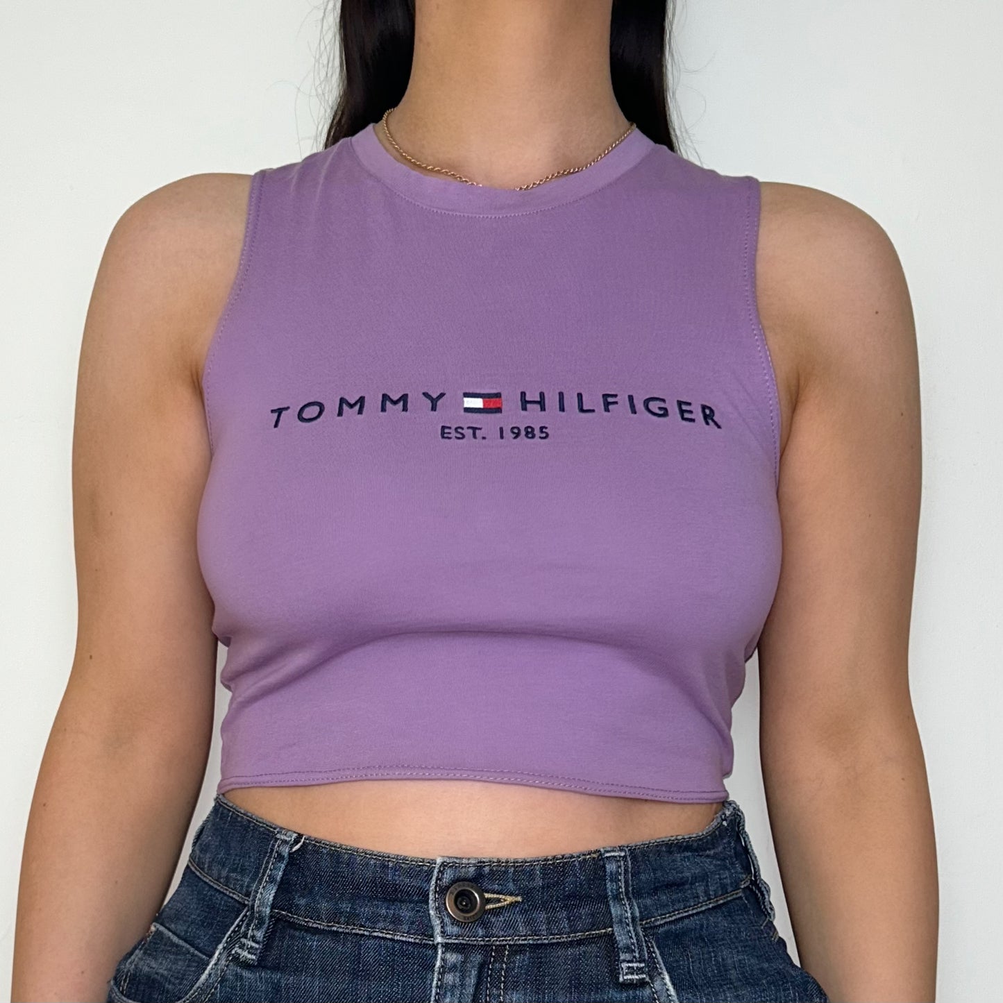 close up of lilac sleeveless crop top with black tommy hilfiger logo shown on a model wearing a denim mini skirt