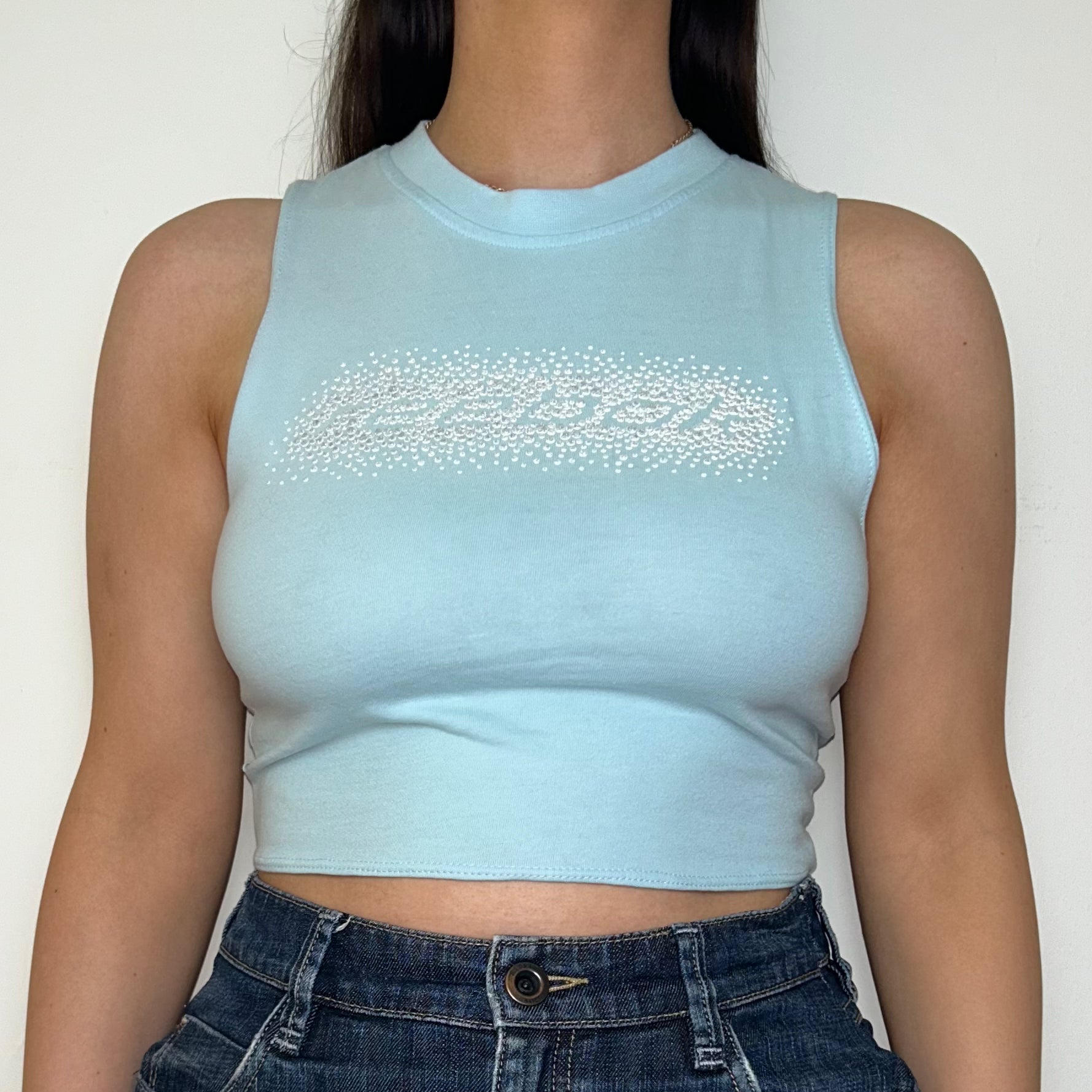 close up of light blue sleeveless crop top with gem reebok logo shown on a model wearing a denim mini skirt