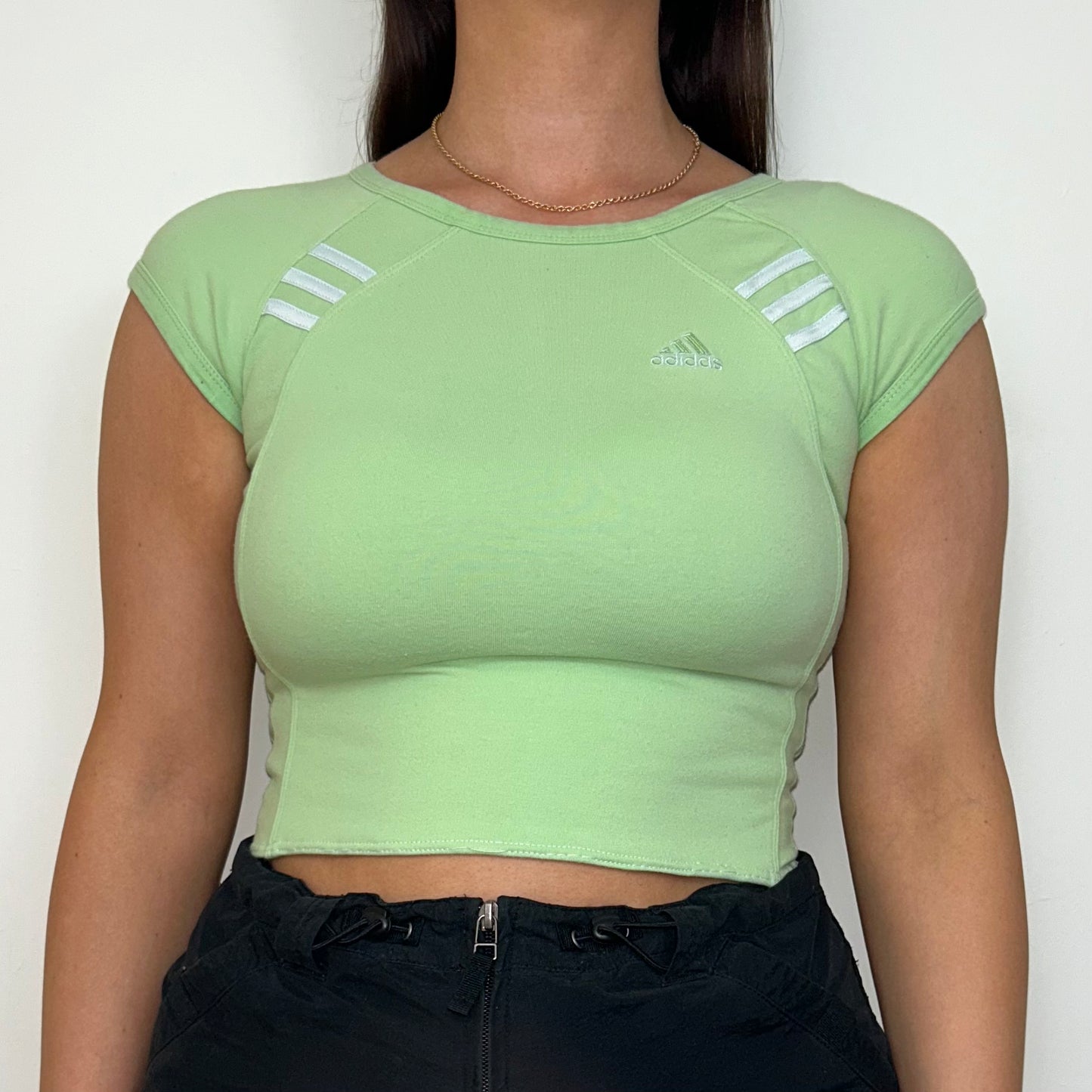 close up of light green short sleeve crop top with white adidas logo shown on a model wearing a black mini skirt
