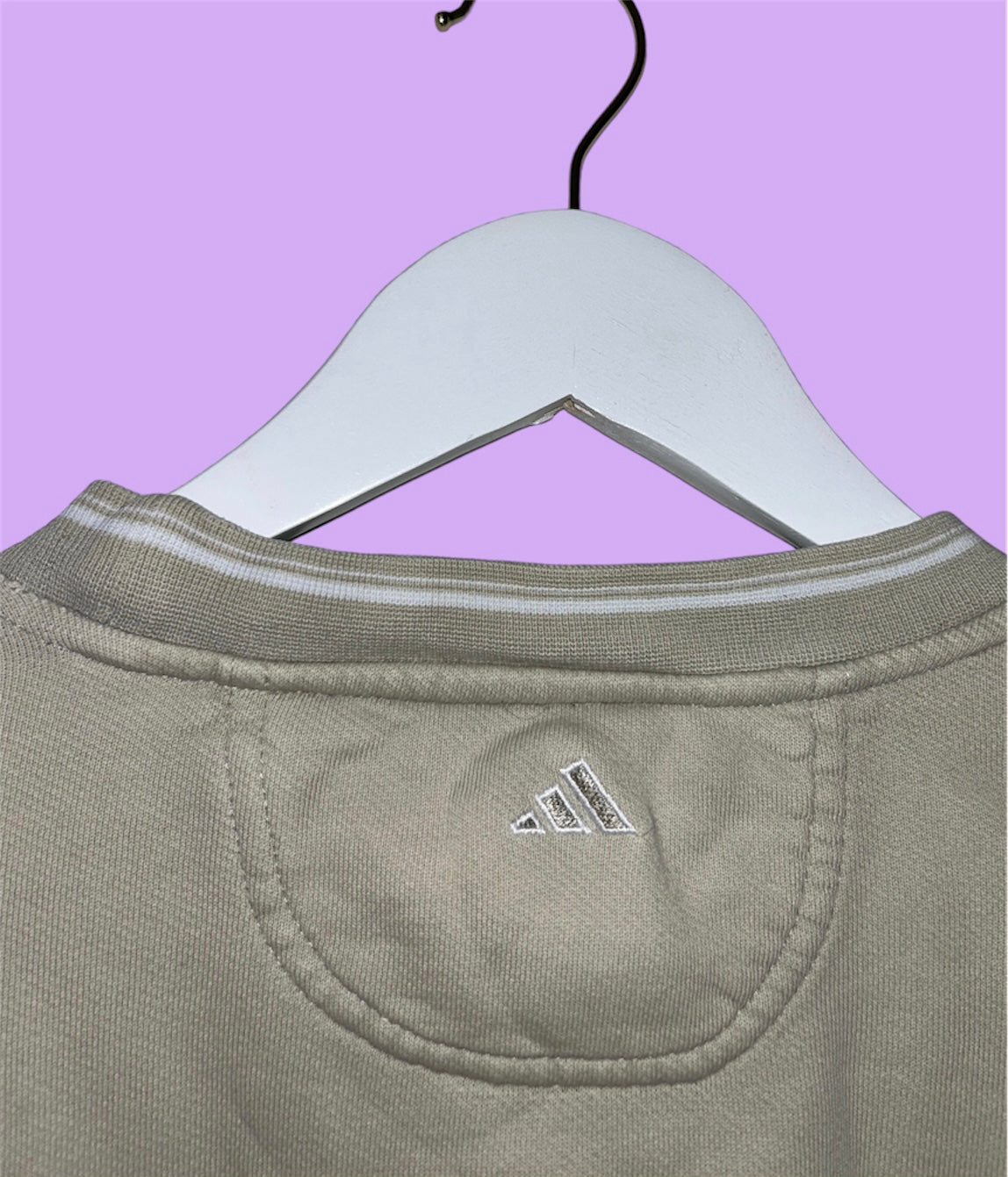 back of a beige sweatshirt with adidas golf logo shown on a lilac background