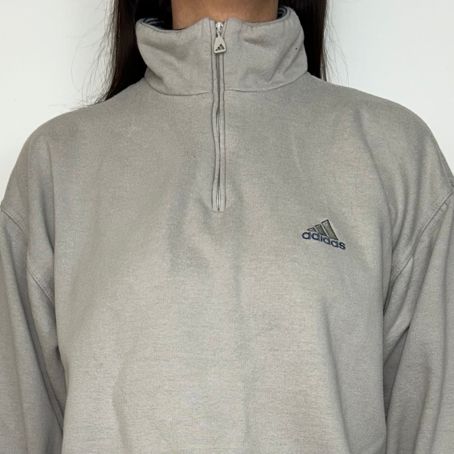close up of beige 1/4 zip sweatshirt with small adidas logo shown on a model 