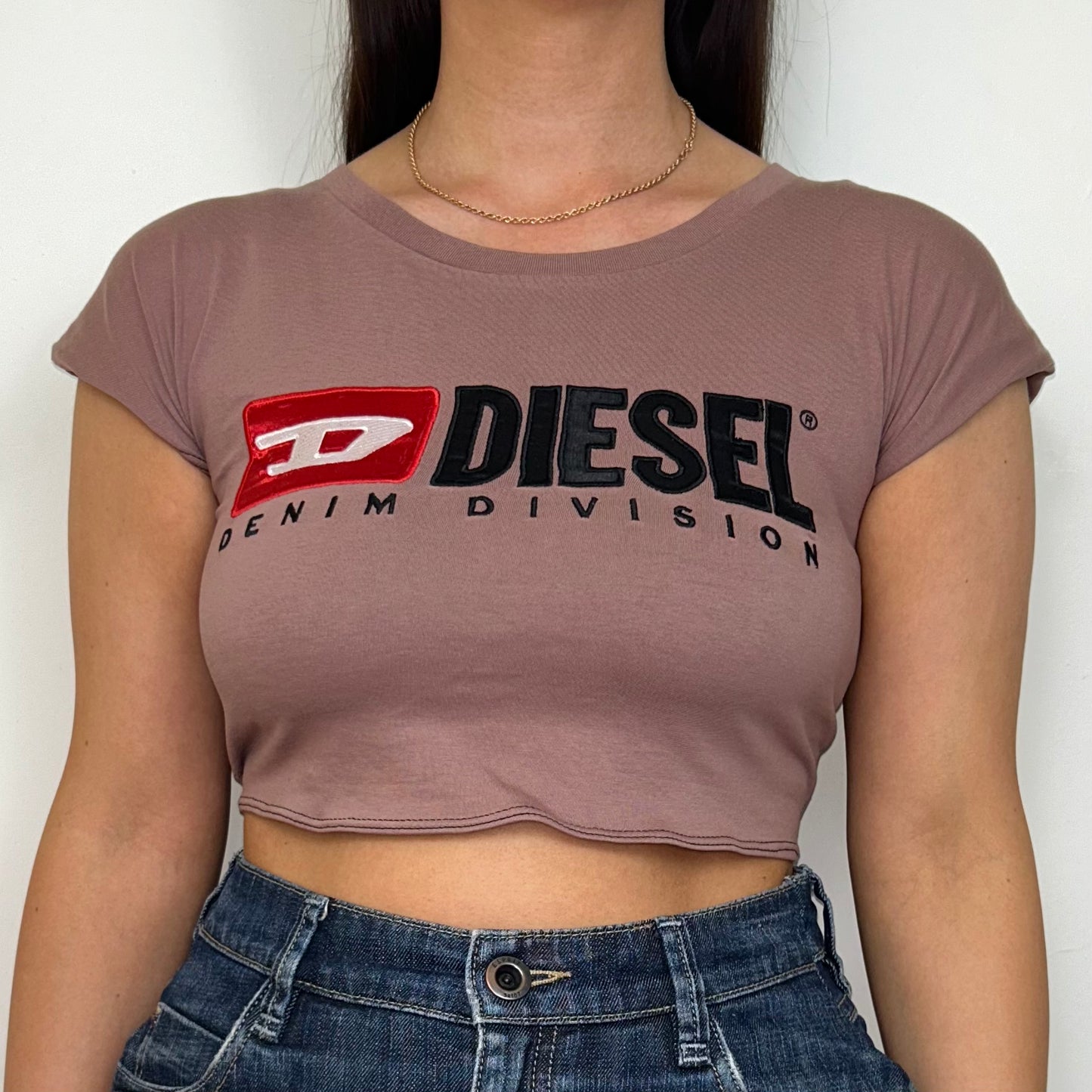 close up of pink short sleeve crop top with black diesel logo shown on a model wearing a denim skirt