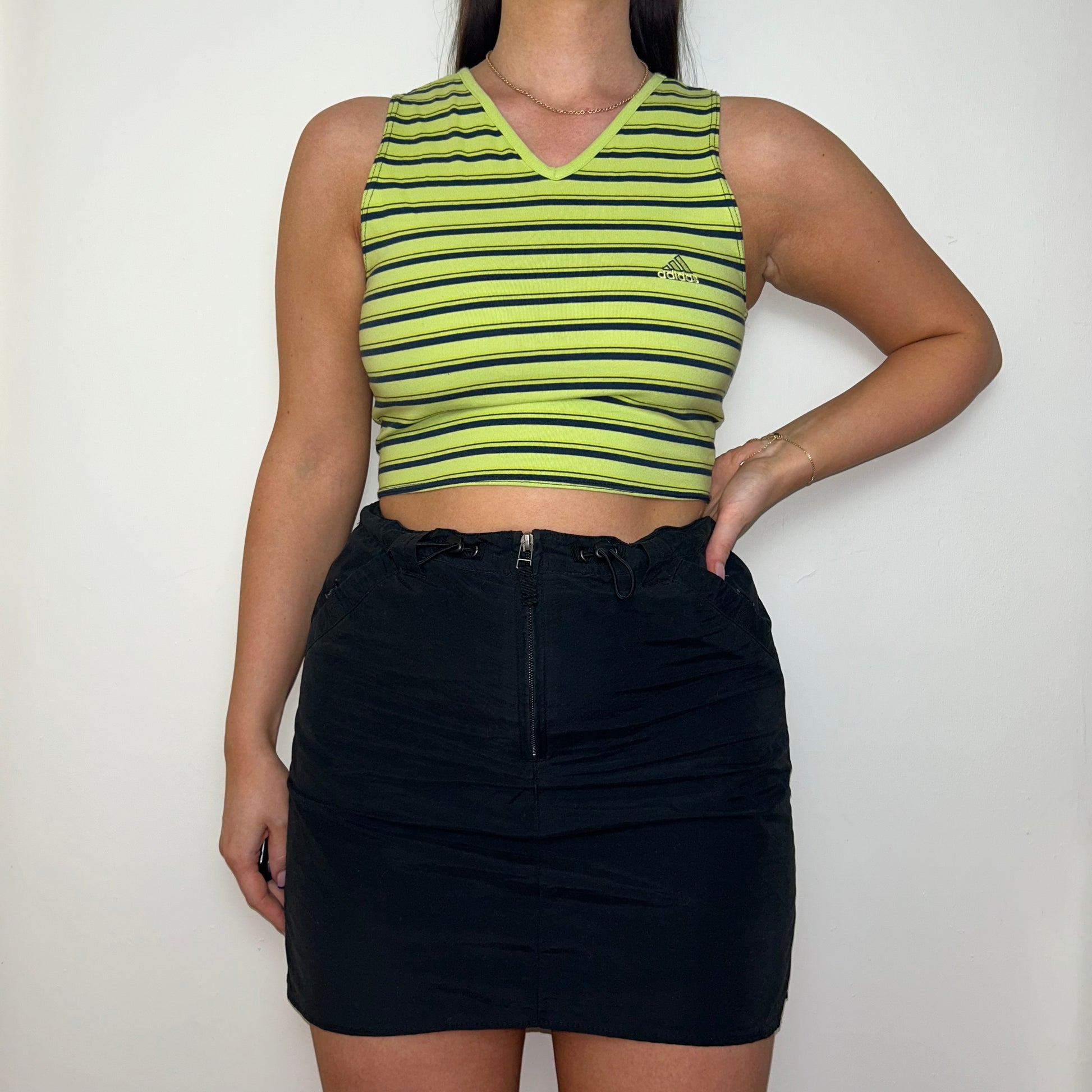 green and black sleeveless crop top with small adidas logo shown on a model wearing a black mini skirt