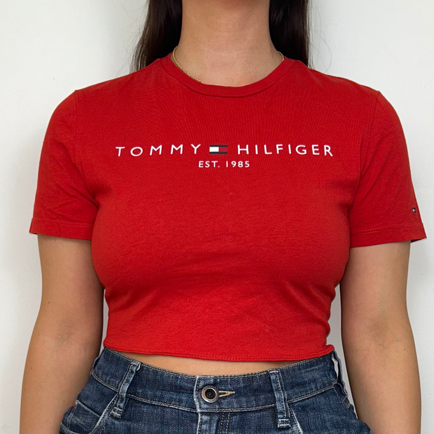 close up of red short sleeve crop top with white tommy hilfiger logo shown on a model wearing a blue denim skirt