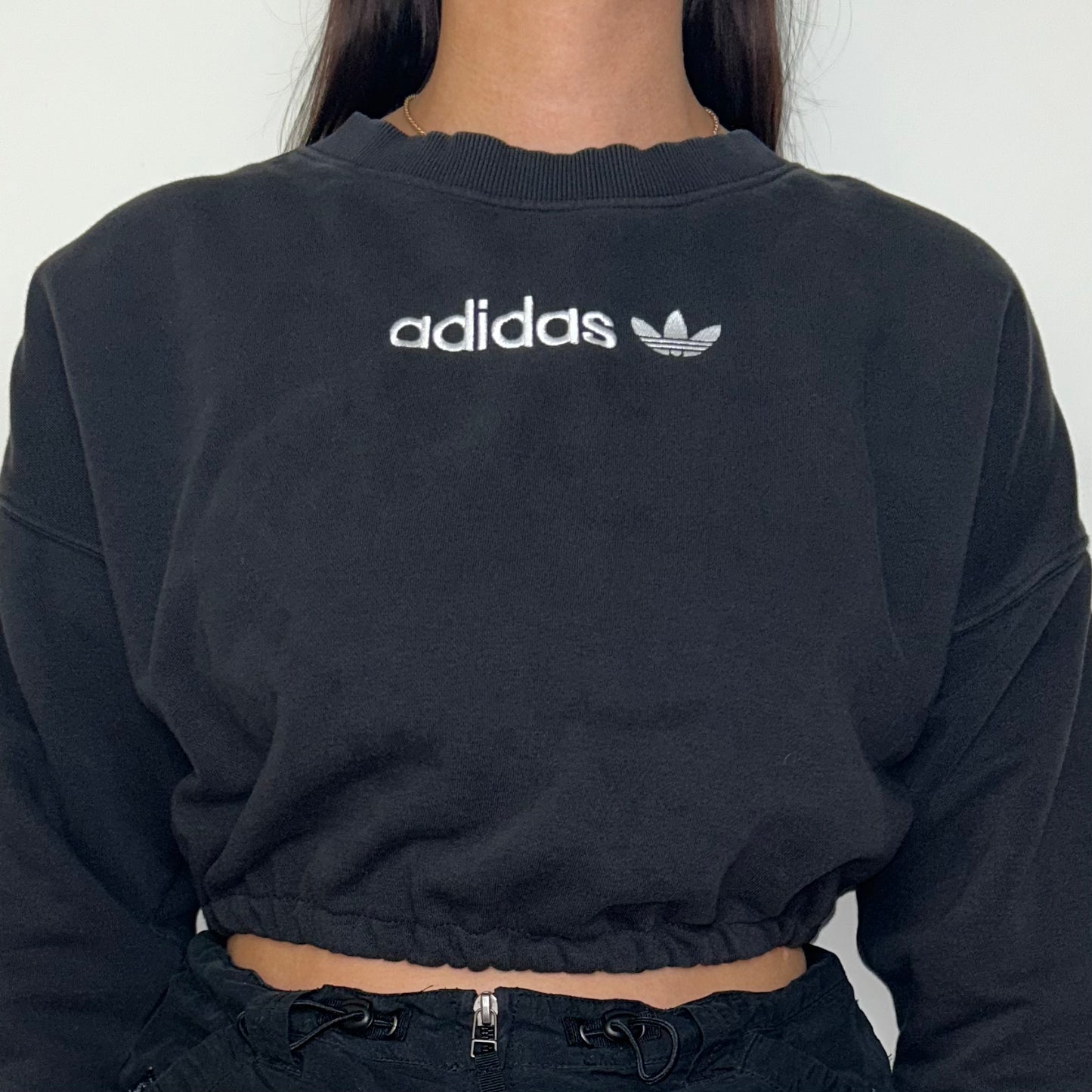 close up of black cropped sweatshirt with white adidas logo shown on a model