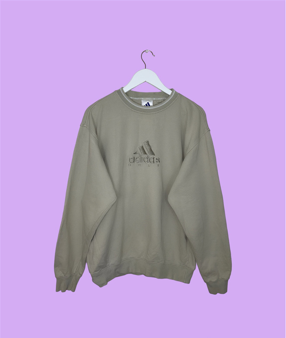 beige sweatshirt with adidas golf logo shown on a lilac background
