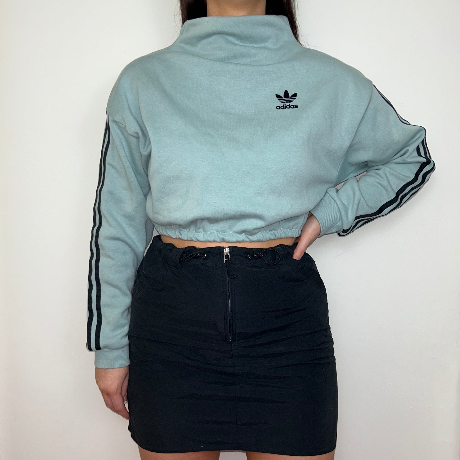 light blue cropped sweatshirt with black adidas logo shown on a model wearing a black mini skirt